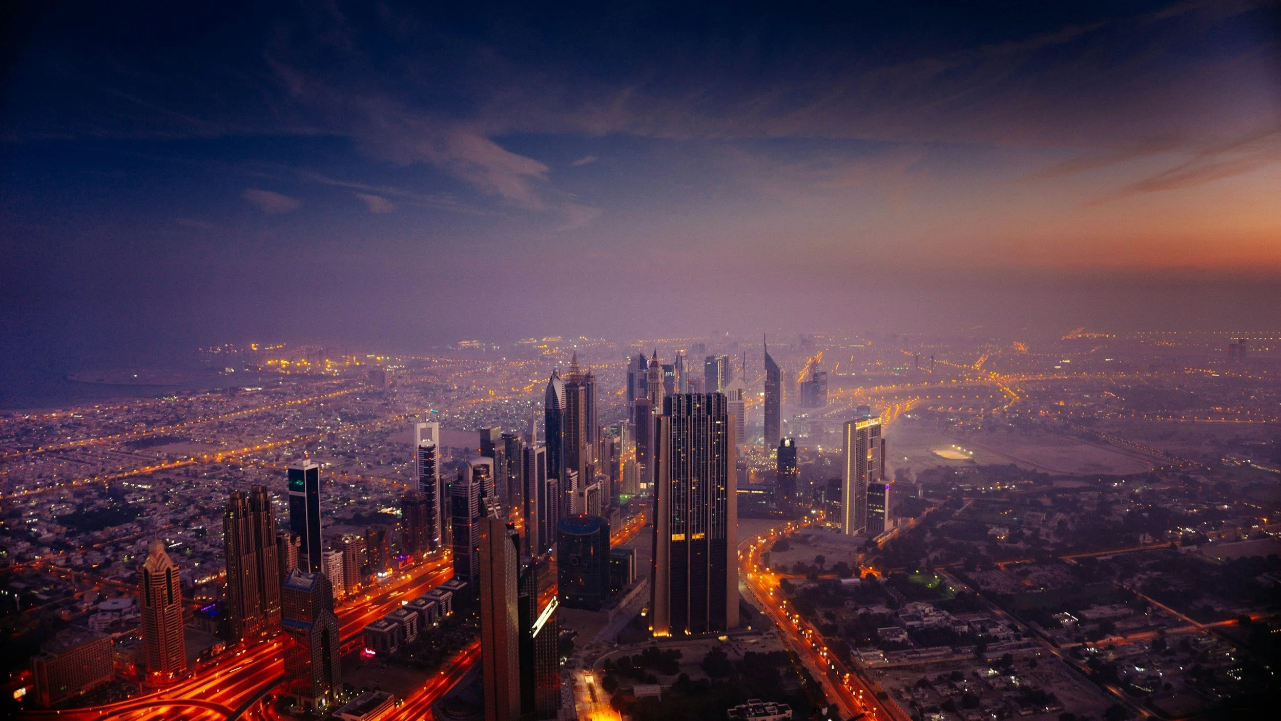 Aerial view of a city skyline at dusk with illuminated skyscrapers and city streets.