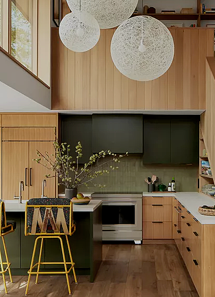 Modern kitchen with wooden cabinets, black upper cabinets, a white stove, and a white marble island with yellow barstools. Hanging pendant lights and a large vase with branches on the counter.