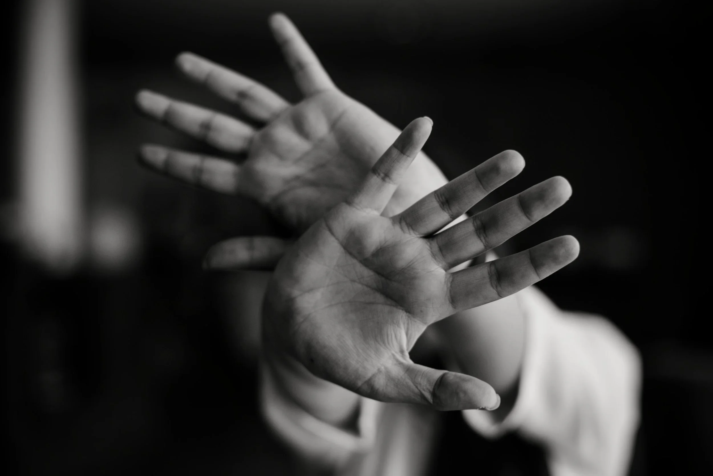 Black-and-white photograph of two hands reaching towards each other with fingers extended, against a dark background.