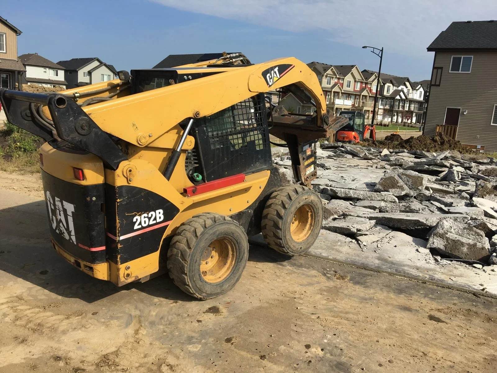 Construction site with trucks and excavators digging and moving earth, surrounded by trees and open land.