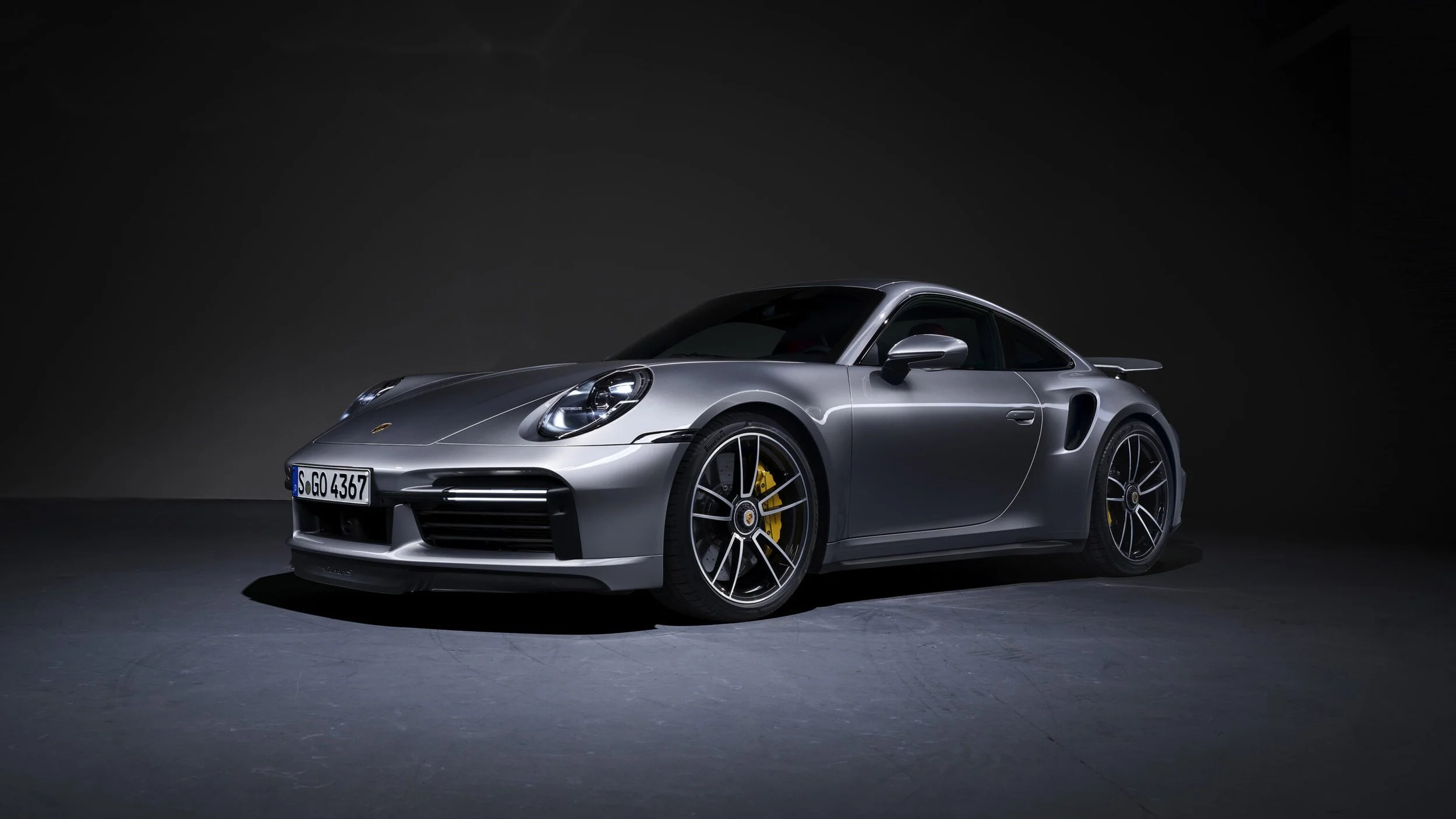 Silver Porsche sports car parked on a dark surface with a dark background.