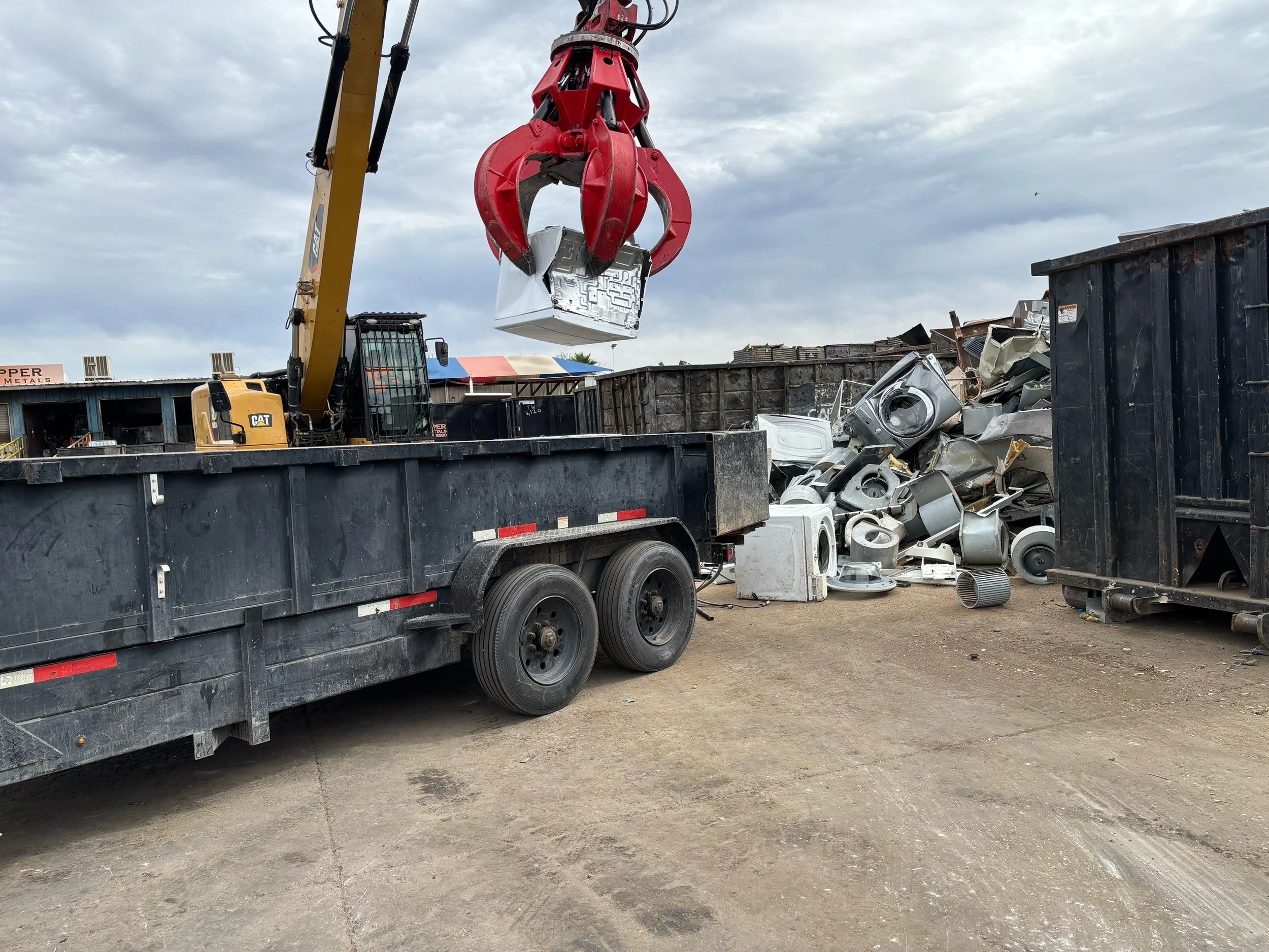 Yellow crane lifting metal scrap at a construction yard surrounded by scrap metal and appliances in Phoenix