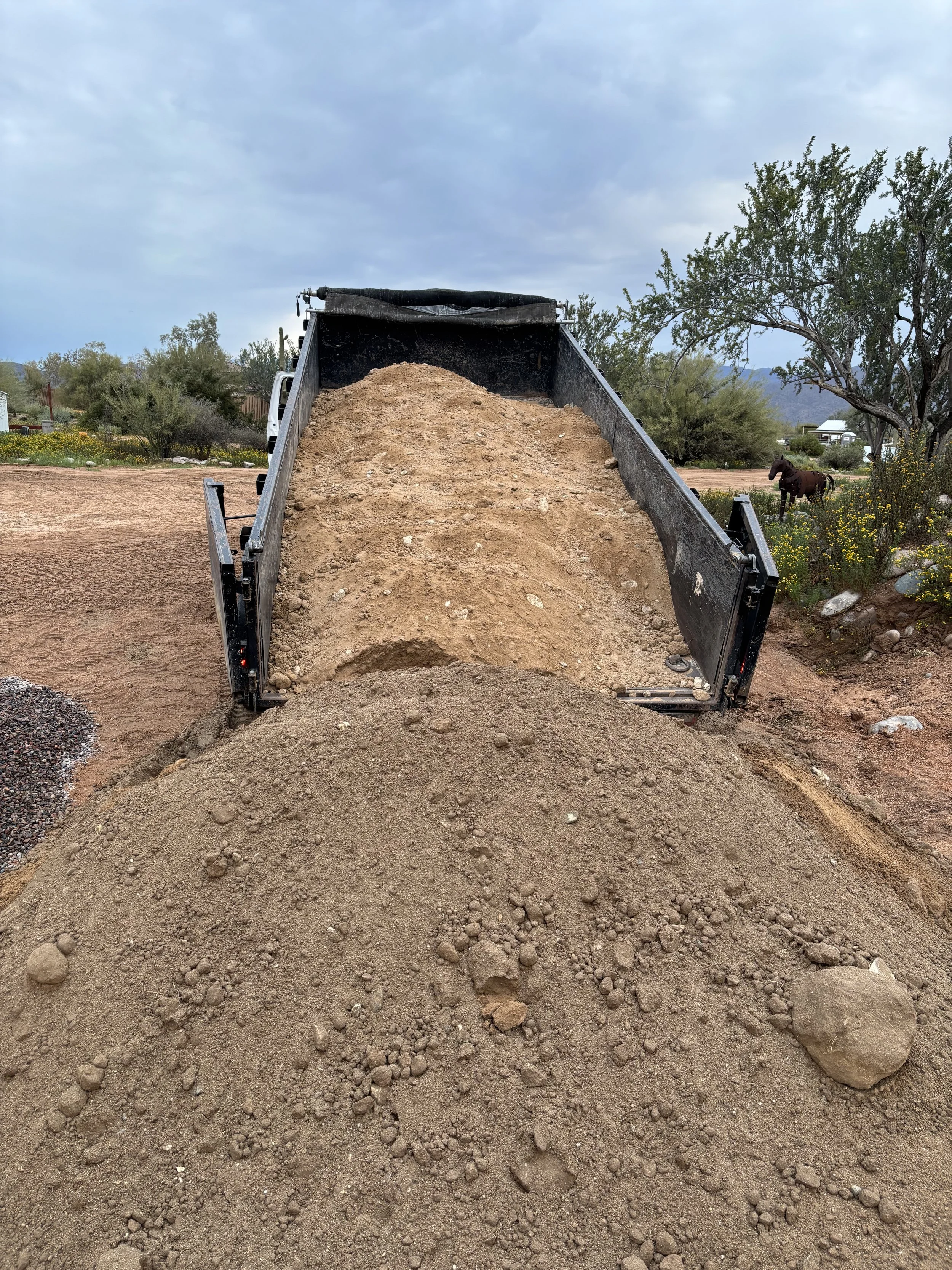 Dump truck unloading soil on a dirt road with mountains in the background in Mesa
