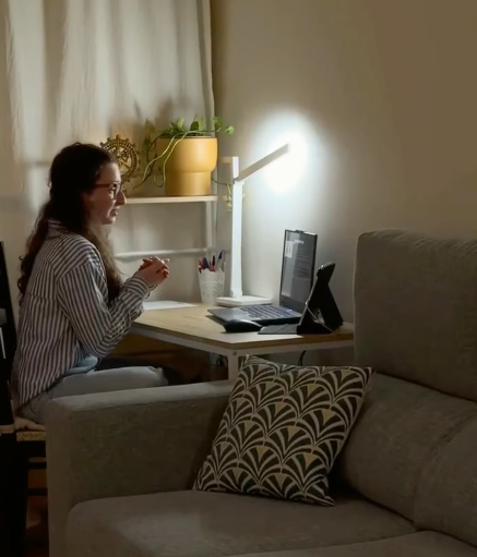 Mulher sentada em uma mesa de trabalho com um computador portátil, lendo ou revisando algo.