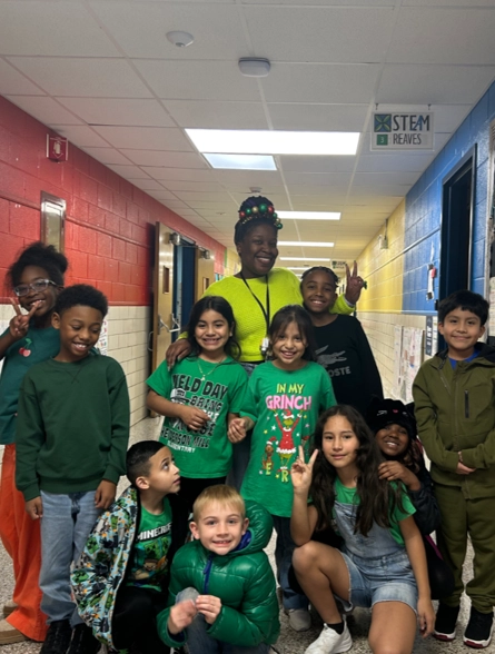 Group of children and a woman in a school hallway, smiling and posing for a photo.