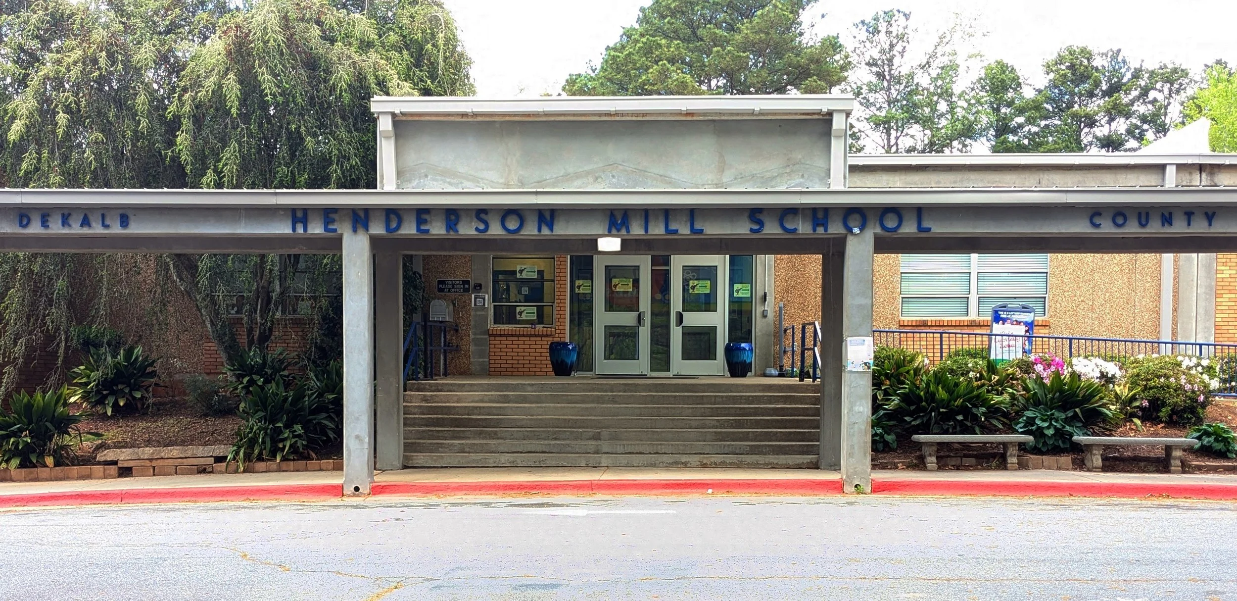 Front view of Henderson Mill School, with stairs leading up to entrance, plants on either side, and a covered walkway.