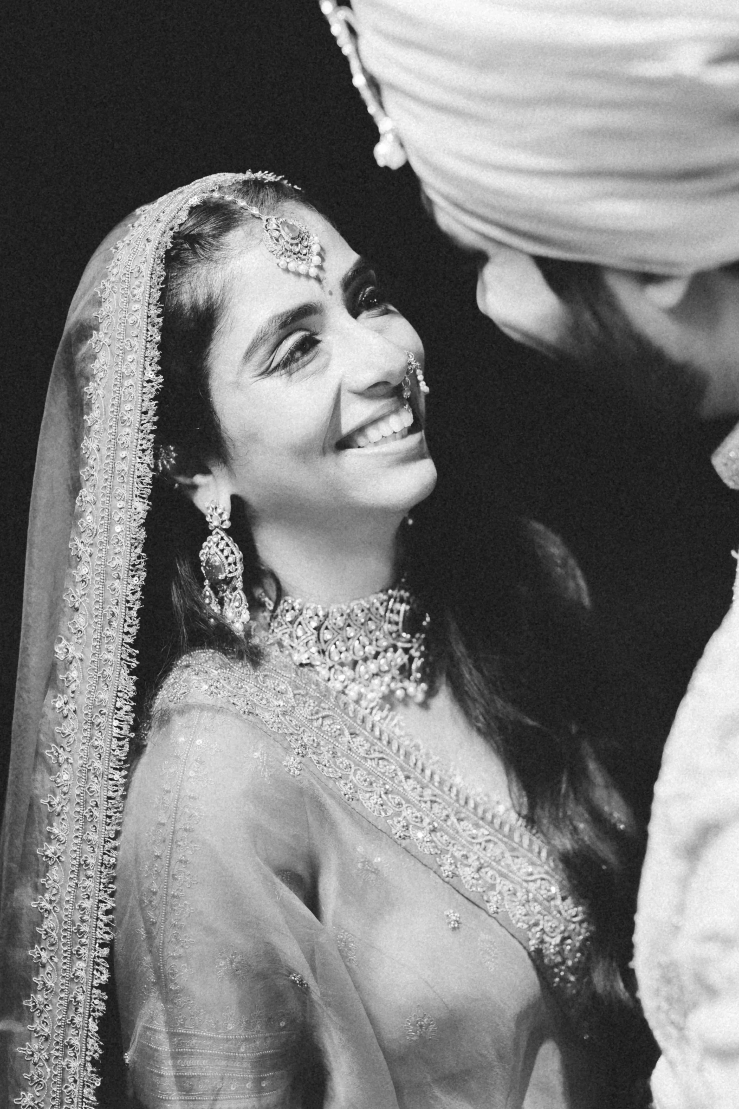 A bride dressed in traditional wedding attire, smiling and looking at the groom during her wedding ceremony.