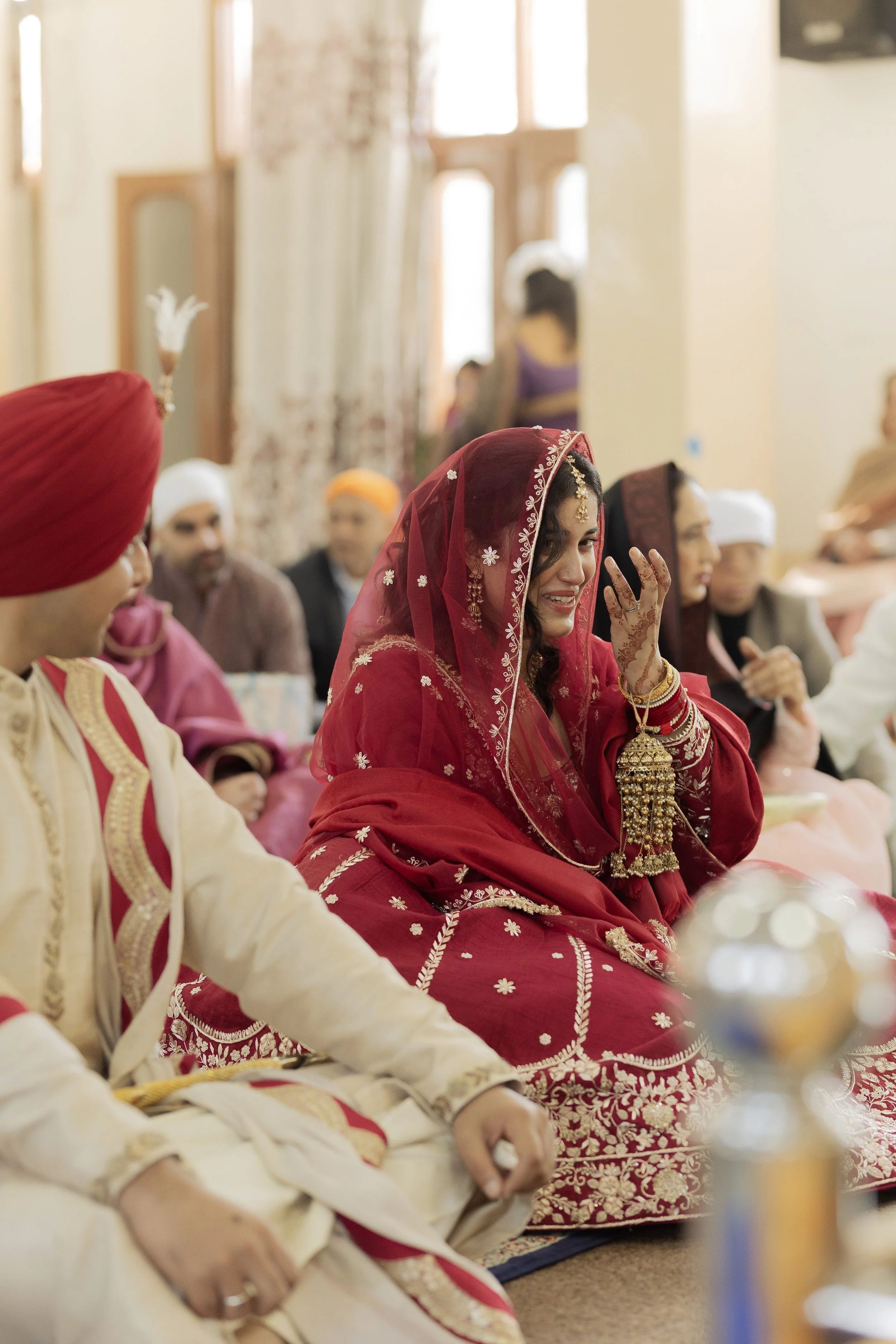 Indian bride dressed in red and gold traditional wedding attire, seated with wedding guests at a ceremony.