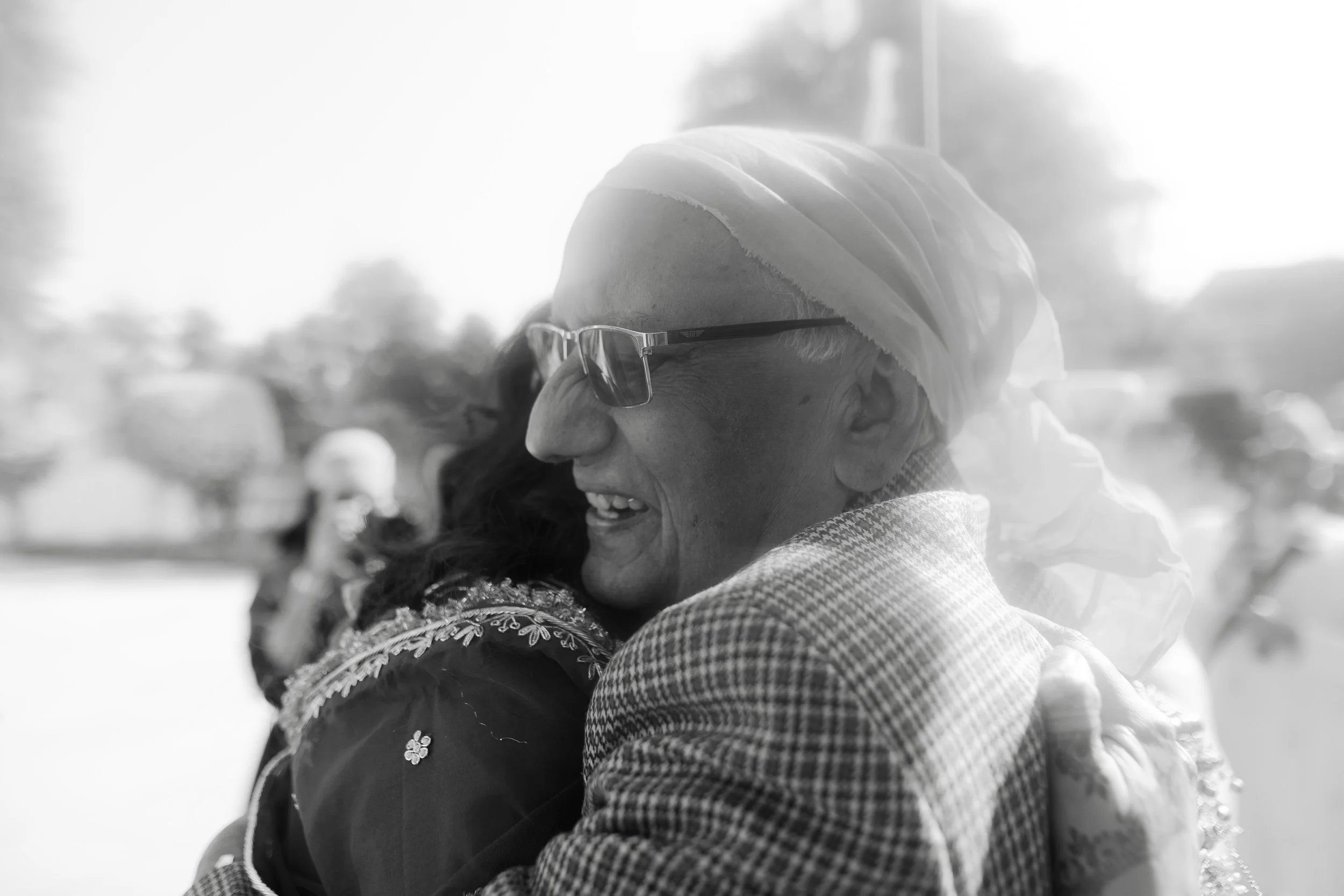 Two people hugging, person on the right with glasses and head wrap, smiling.