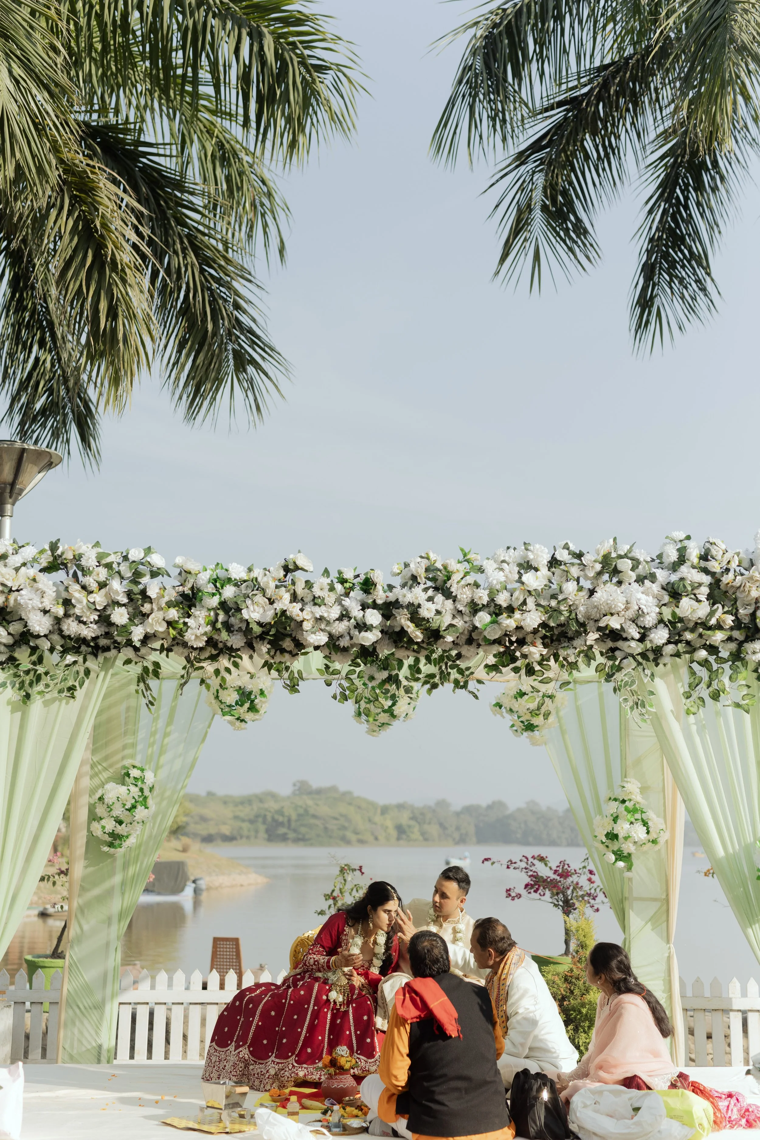 Indian wedding ceremony outdoors near water with floral decorations.