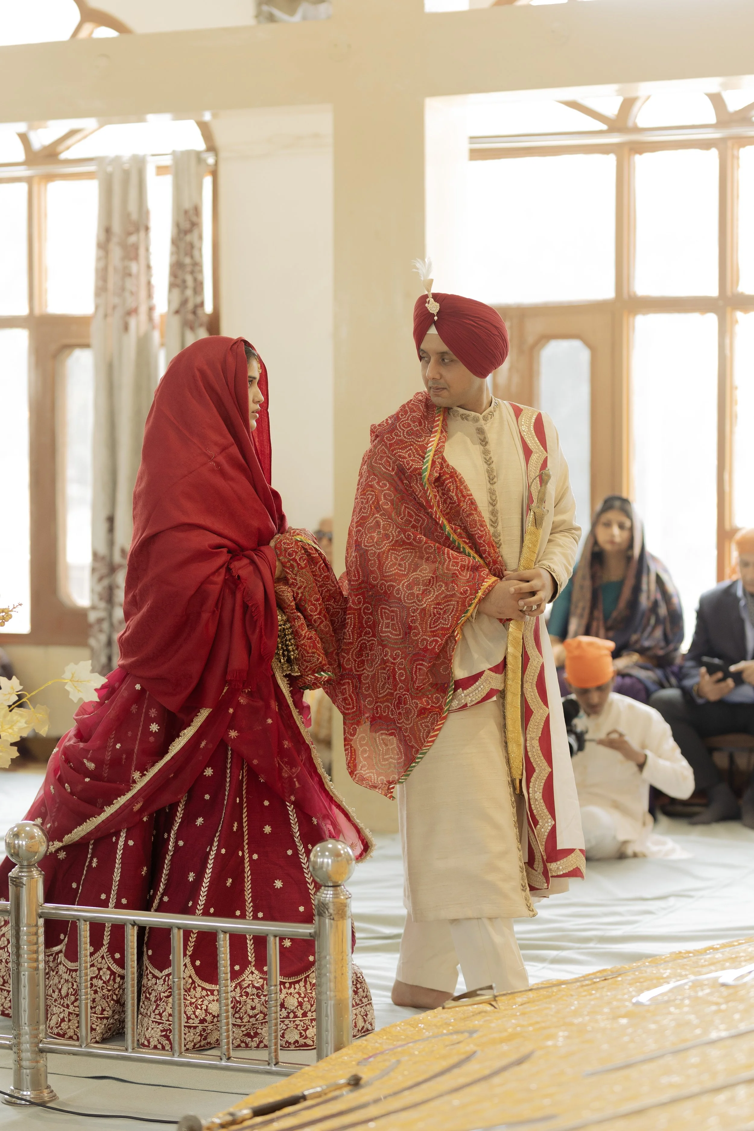 Indian bride and groom dressed in traditional wedding attire, standing in a decorated room during a wedding ceremony.