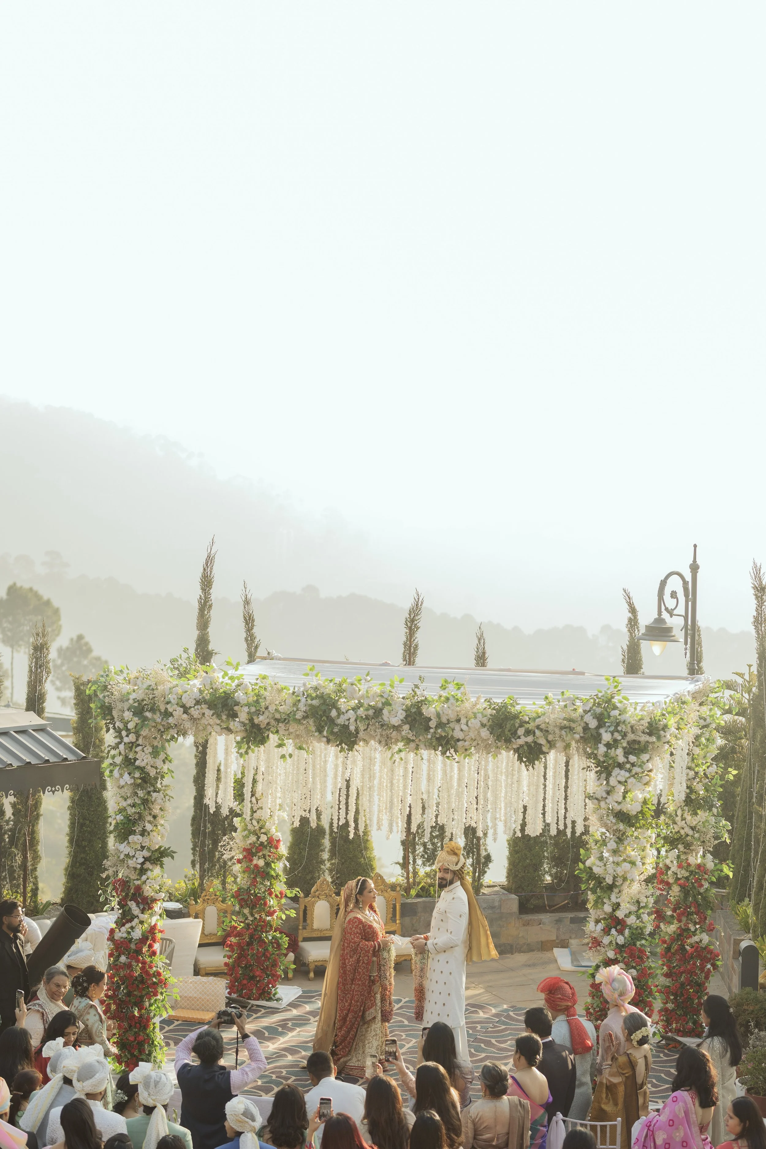 An outdoor wedding ceremony with a floral arch, a bride and groom, and guests seated while taking photos.