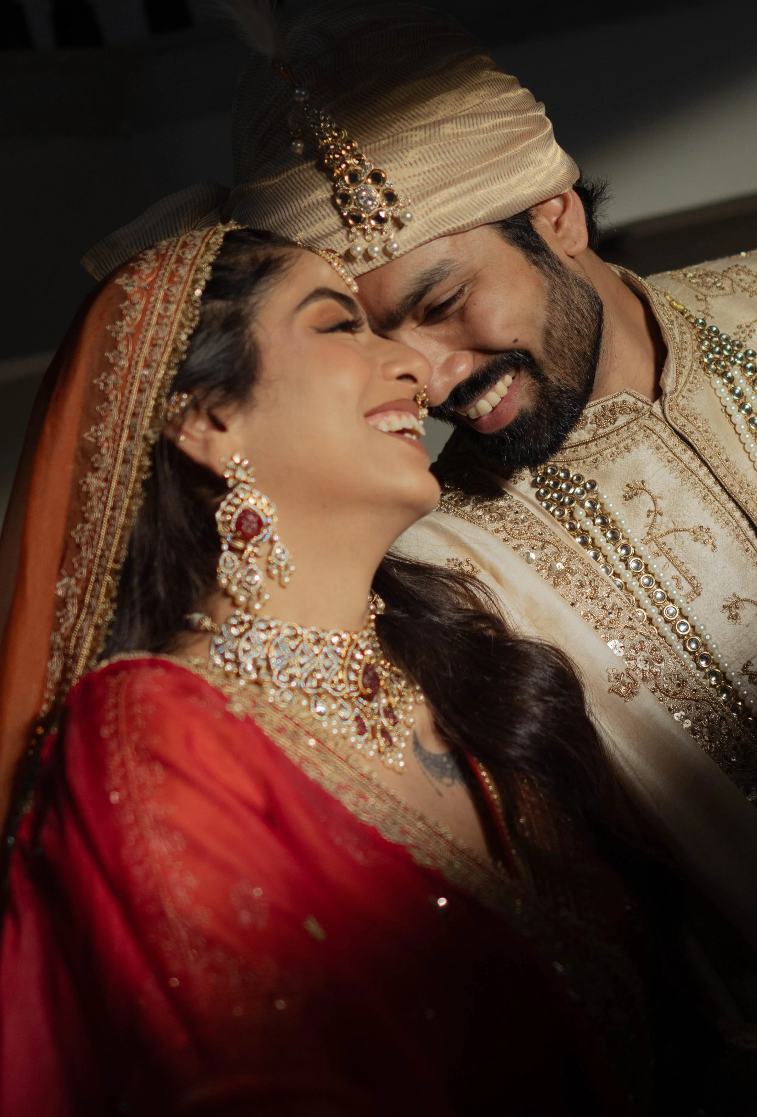 A couple dressed in traditional Indian wedding attire sharing a joyful moment, close-up of their faces with happy expressions.