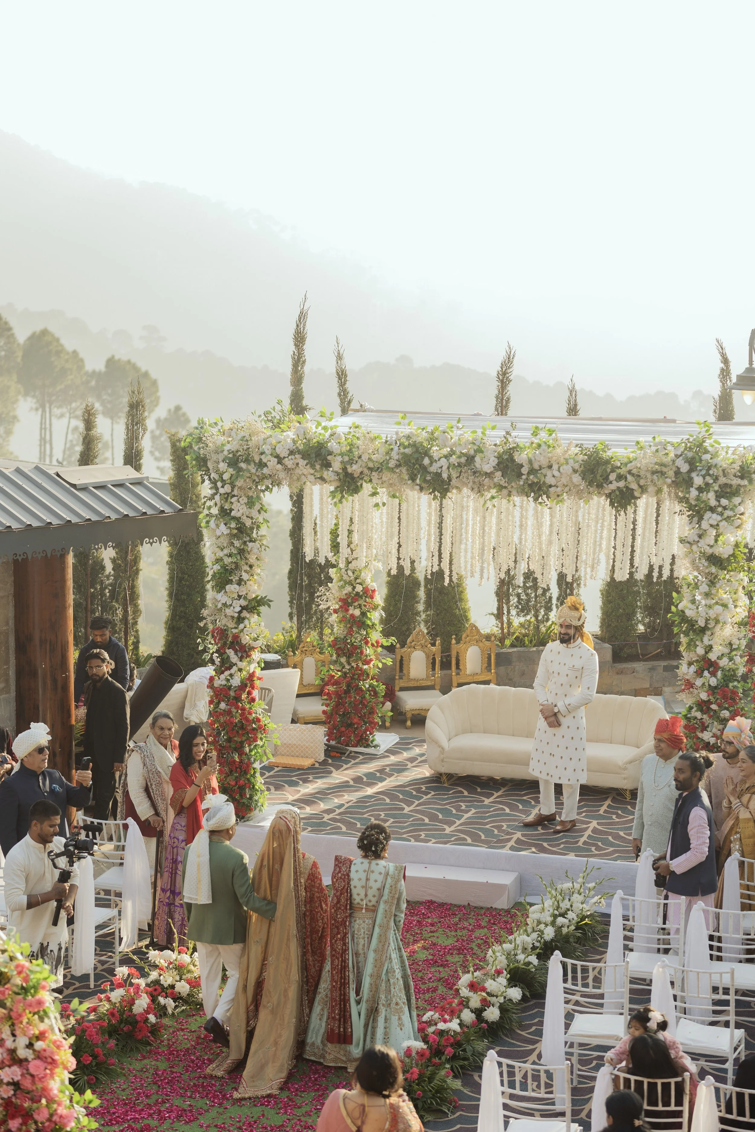A traditional Indian wedding ceremony with floral decorations, a stage, and guests dressed in colorful attire.