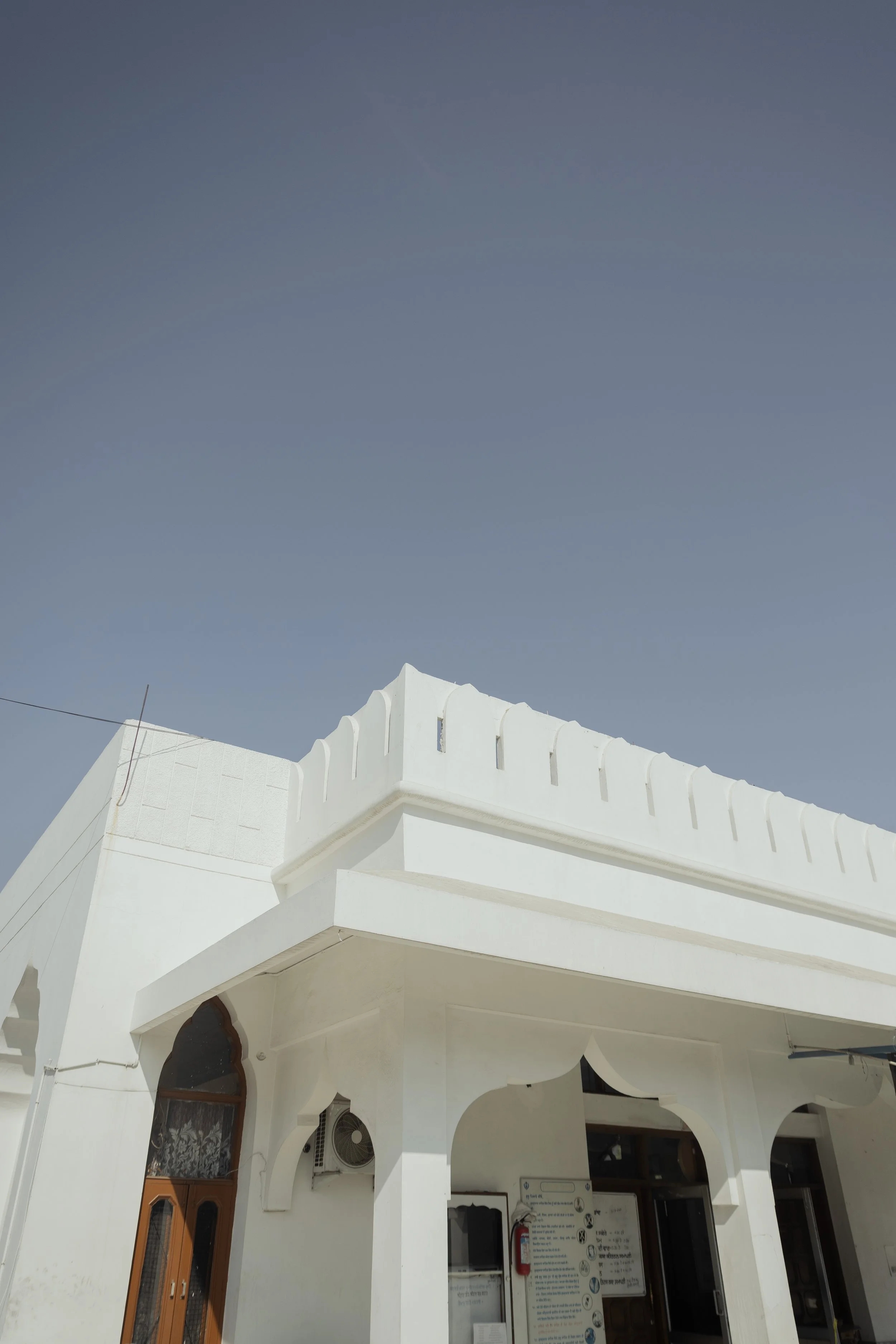 A white building with architectural details, arched windows, and an air conditioning unit under a clear blue sky.