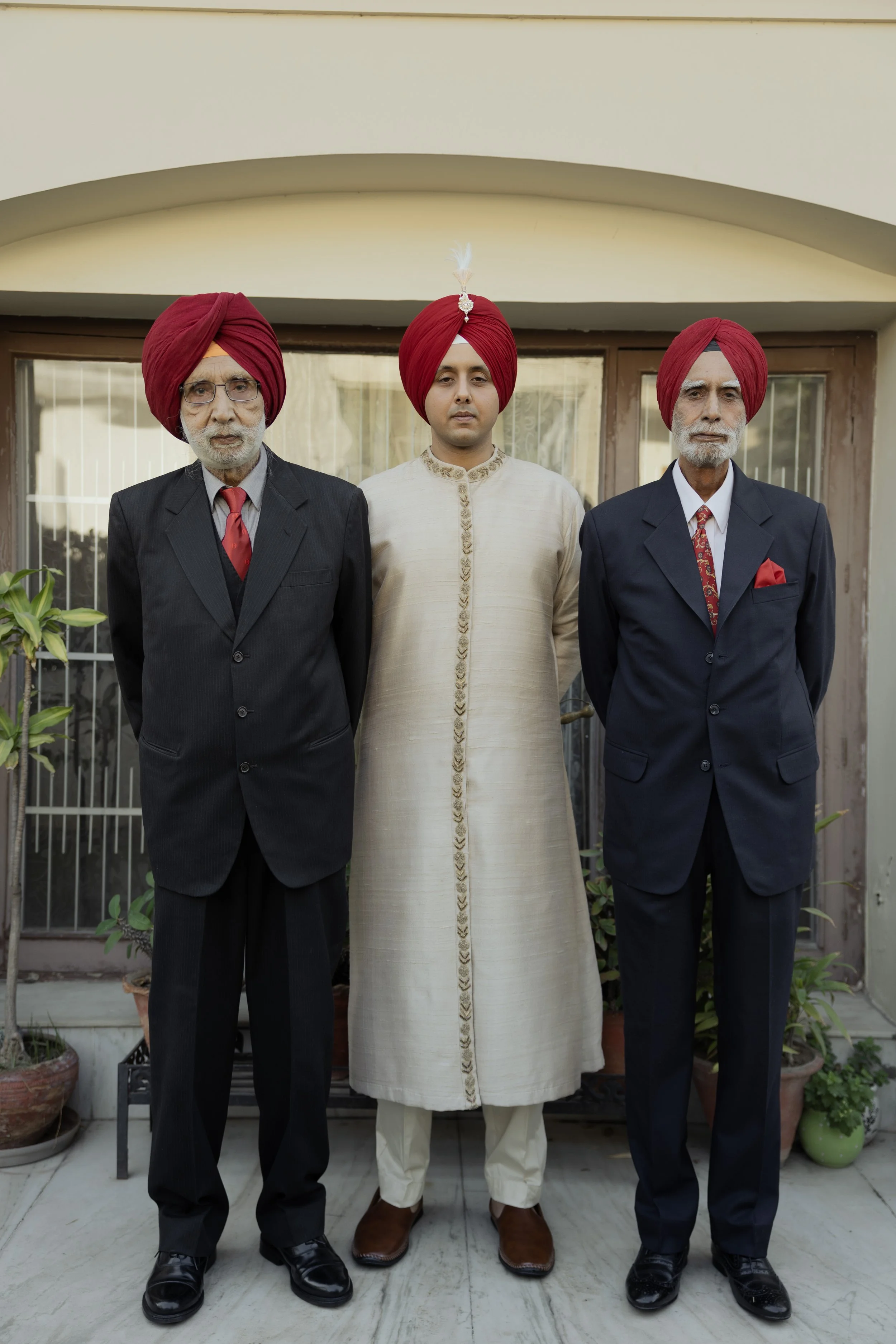 Three men wearing traditional Sikh turbans and formal attire standing outside a house.