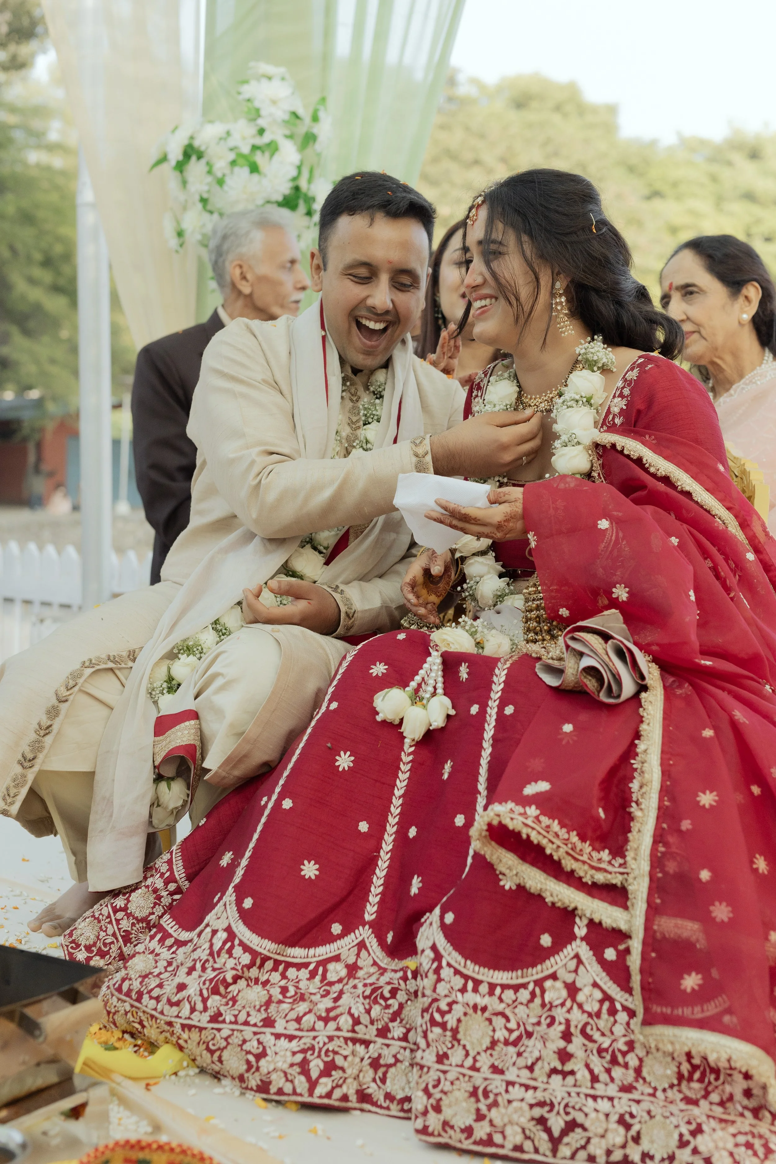 Hindu wedding ceremony with bride and groom in traditional attire, exchanging floral garlands, surrounded by family members.