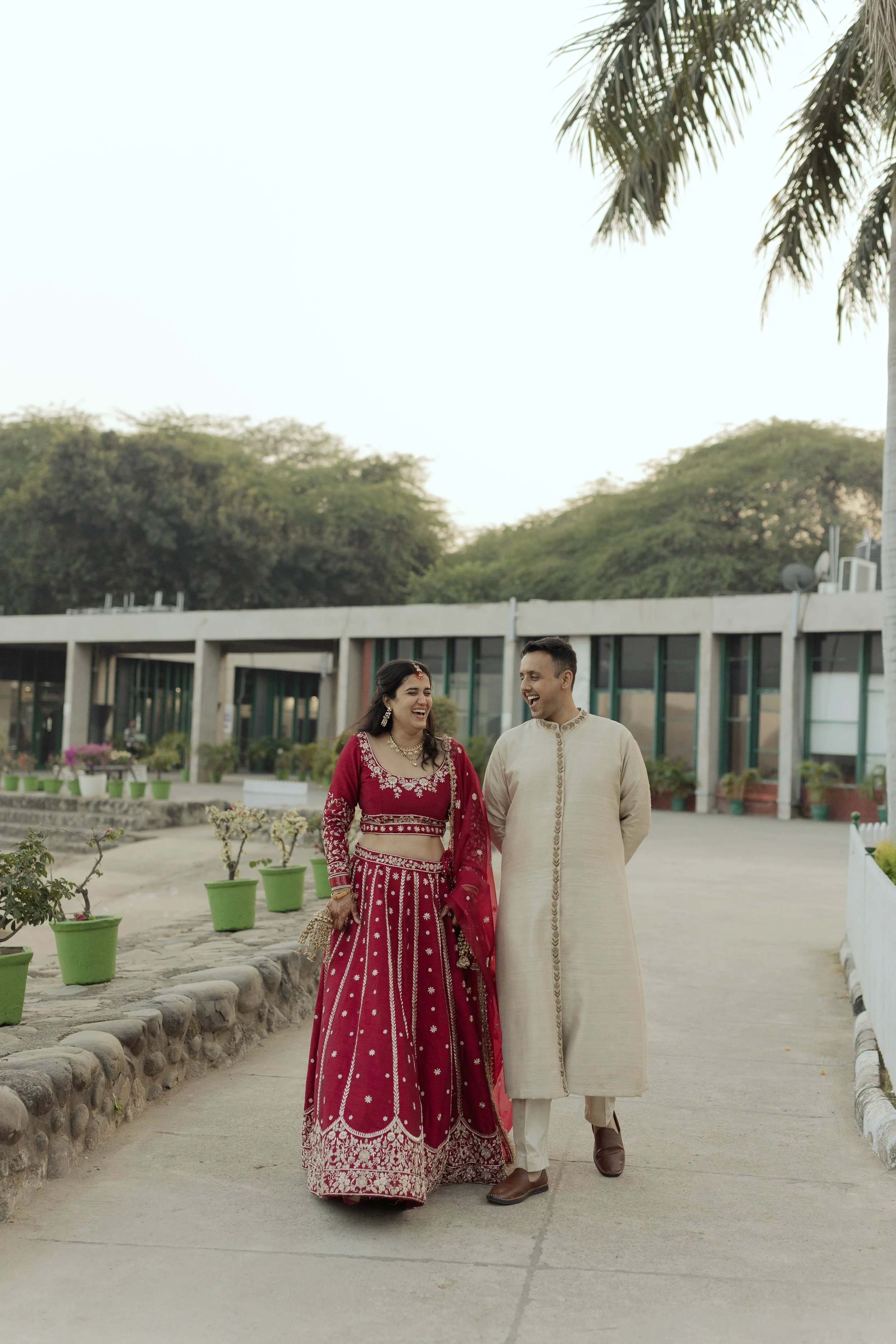 A couple dressed in traditional Indian attire walking outdoors, smiling and laughing.