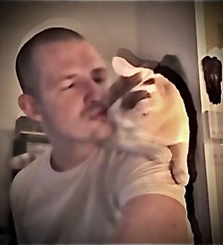 A man holding and kissing a bulldog in a home interior.