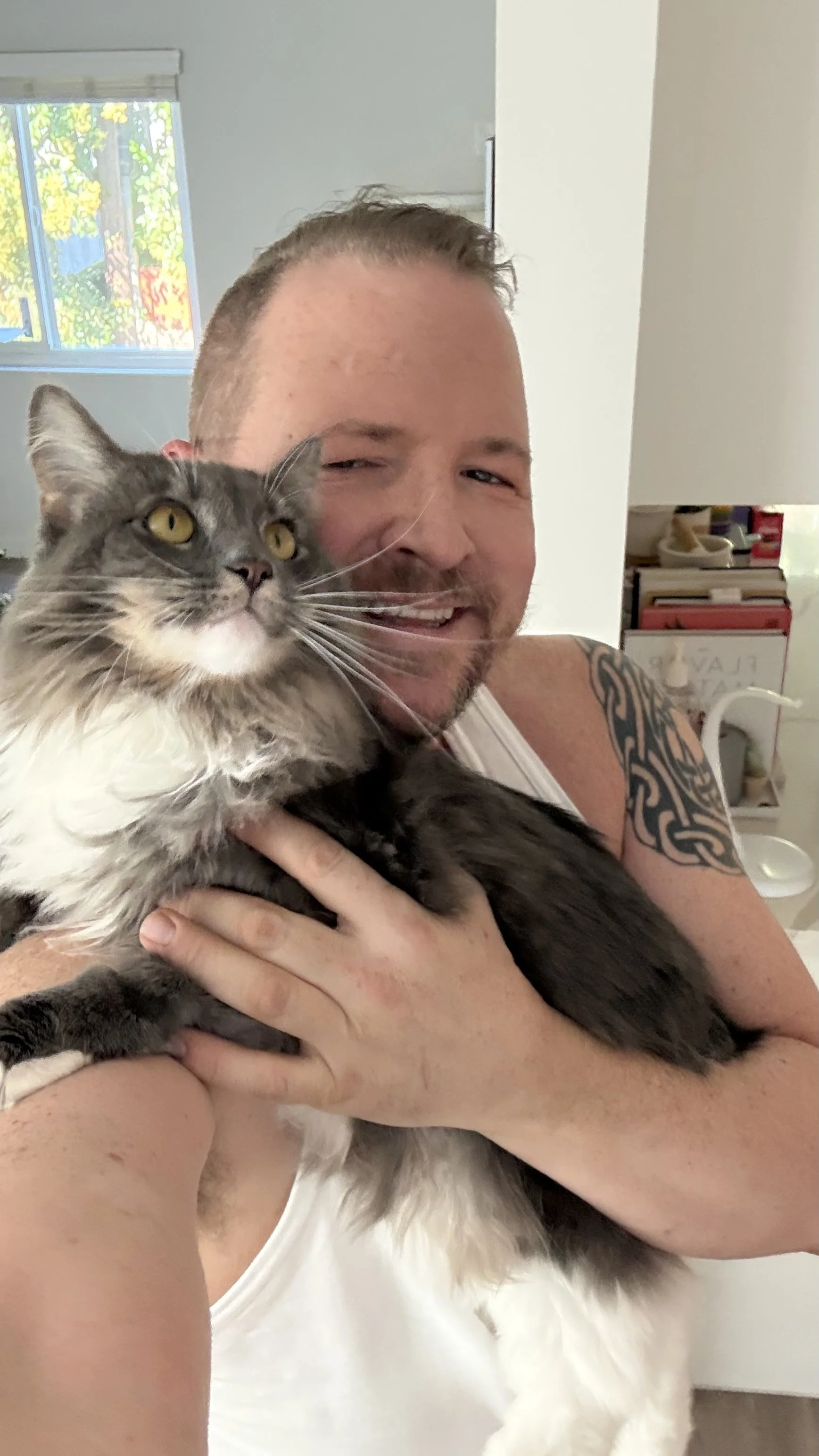 A man holding a gray and white fluffy cat indoors, smiling at the camera.