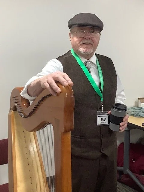 A man wearing a hat leaning on a harp while holding a coffee cup