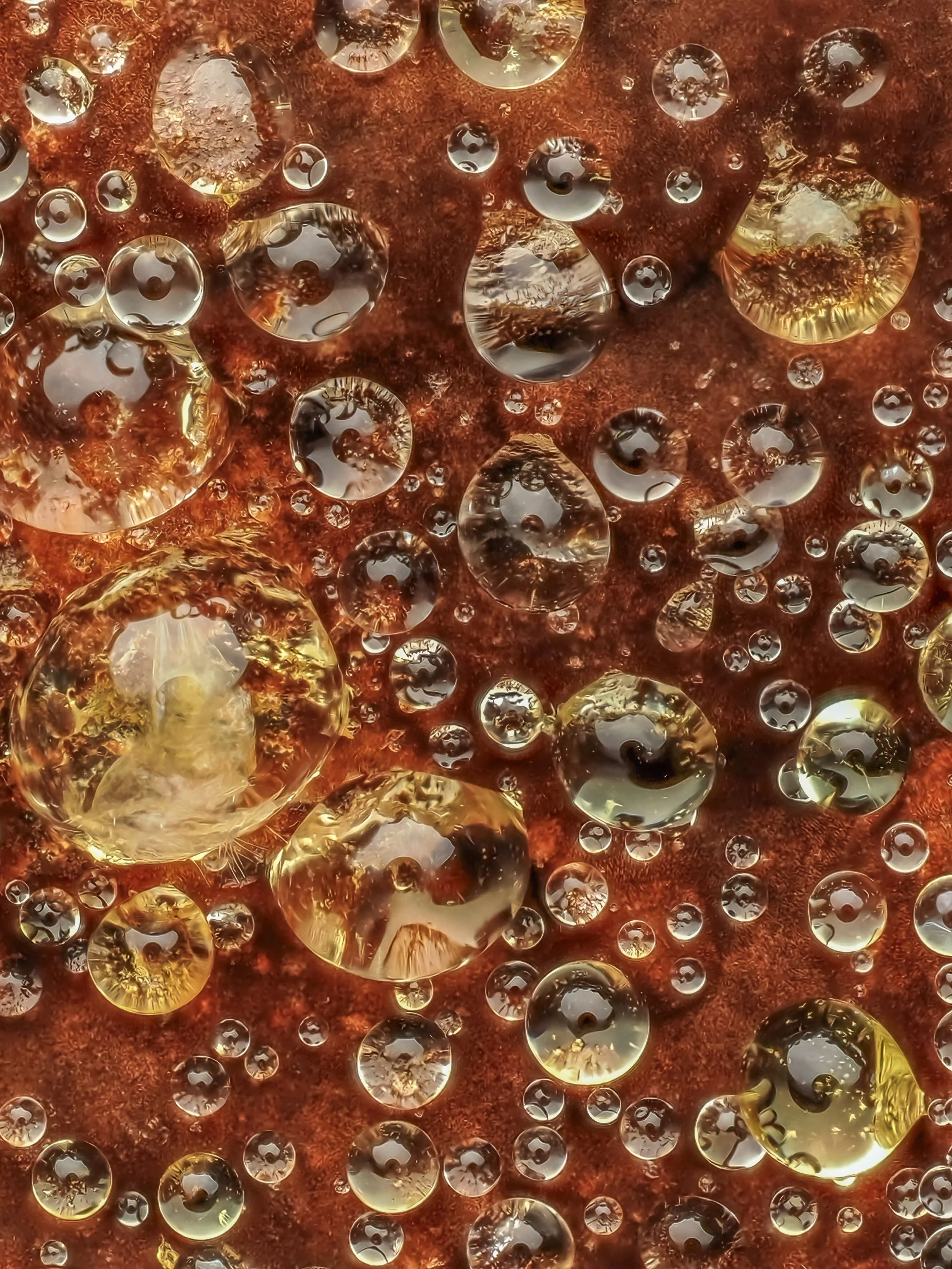 Close-up of numerous water droplets on a textured reddish-brown surface, with reflections and golden hues.