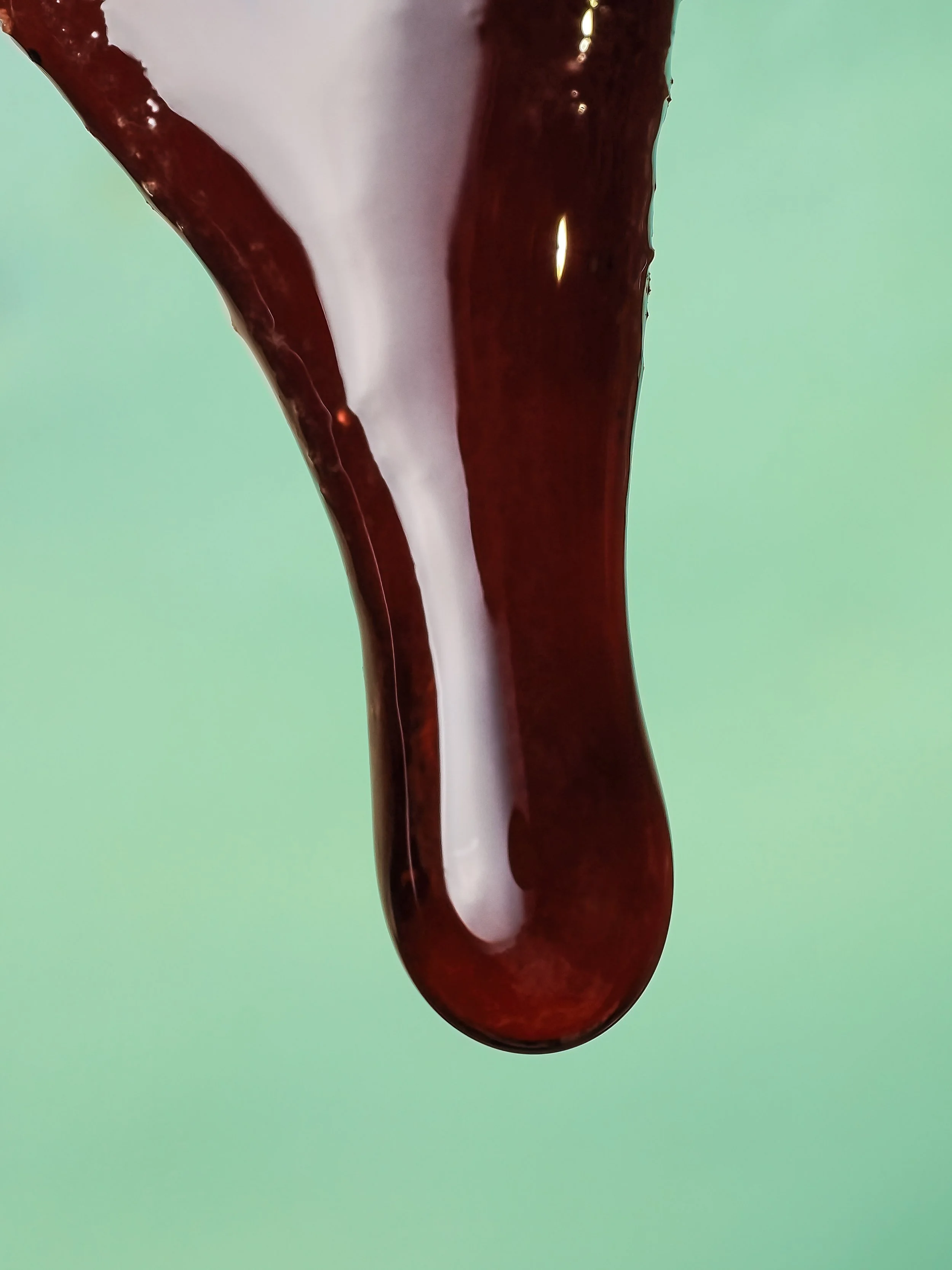 Close-up of a drop of red liquid from beefsteak mushroom, hanging against a light green background.