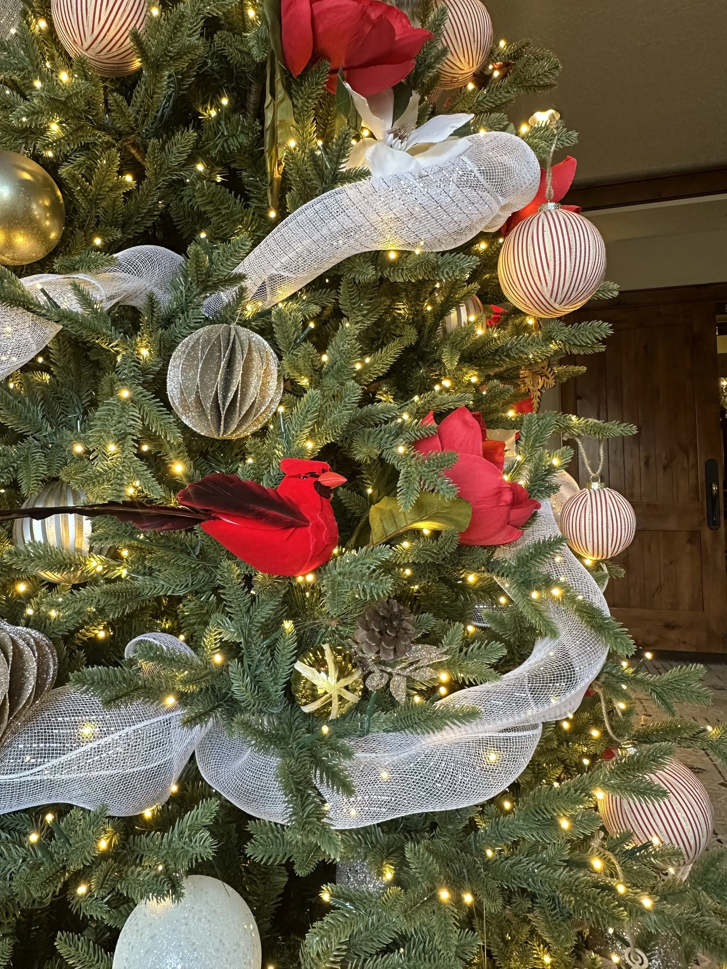 Close-up of a decorated Christmas tree featuring red, white, and gold ornaments, red poinsettia flowers, shimmering white ribbon, and warm white string lights.