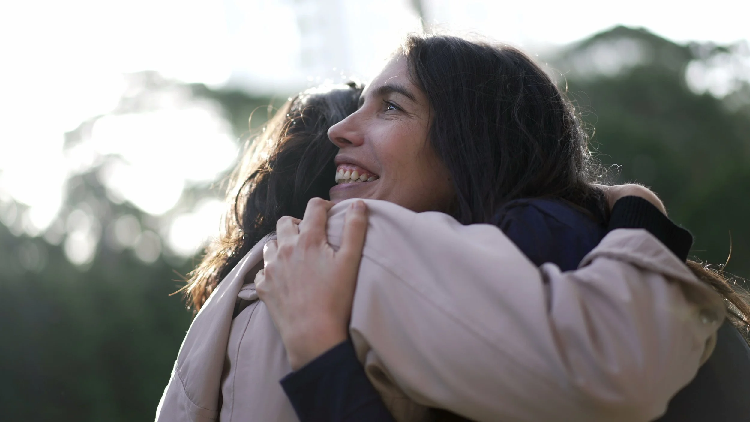 woman with long brown hair hugging another person
