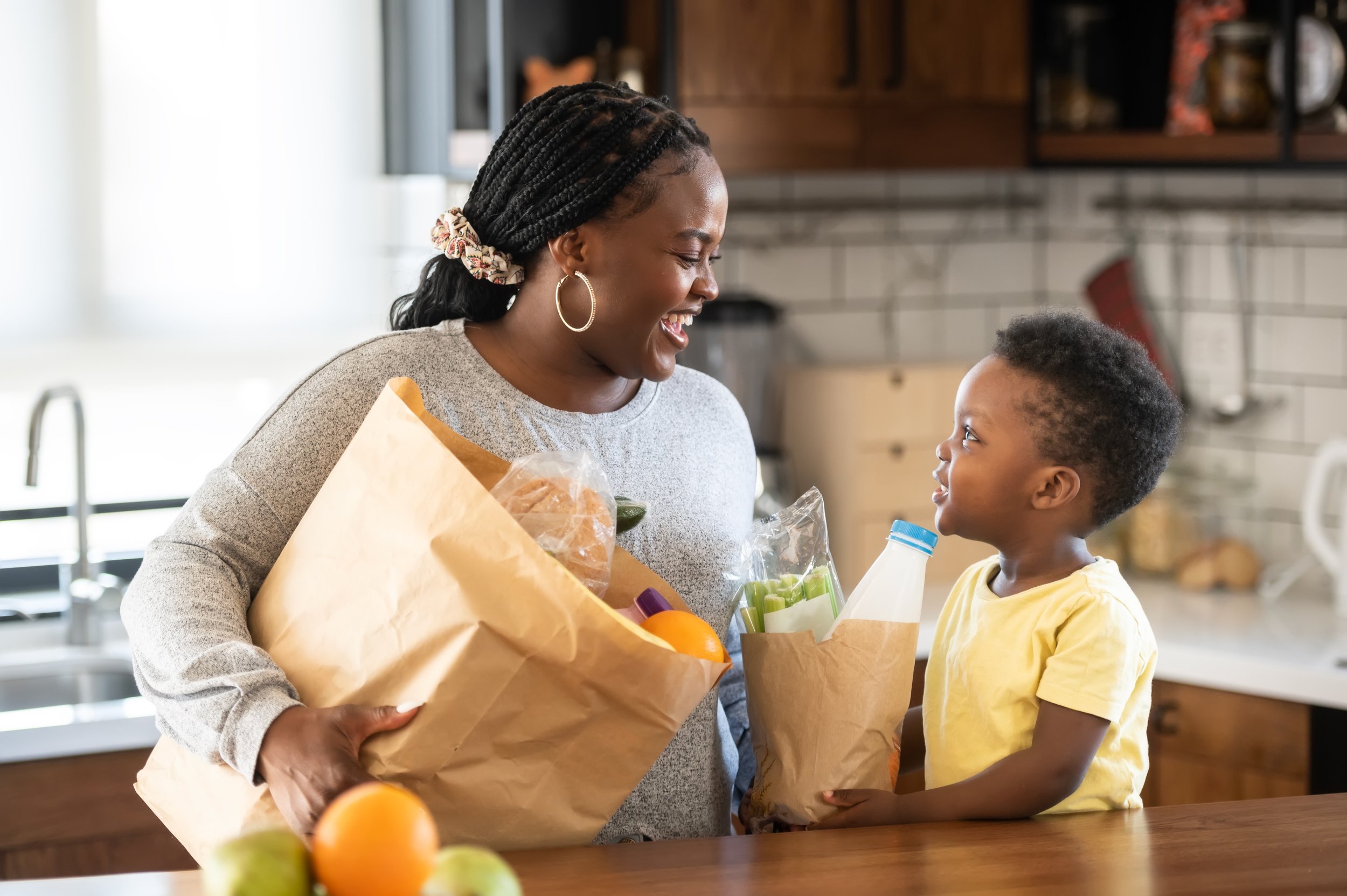 African American mother and young son in a kitchen with two bags of groceries