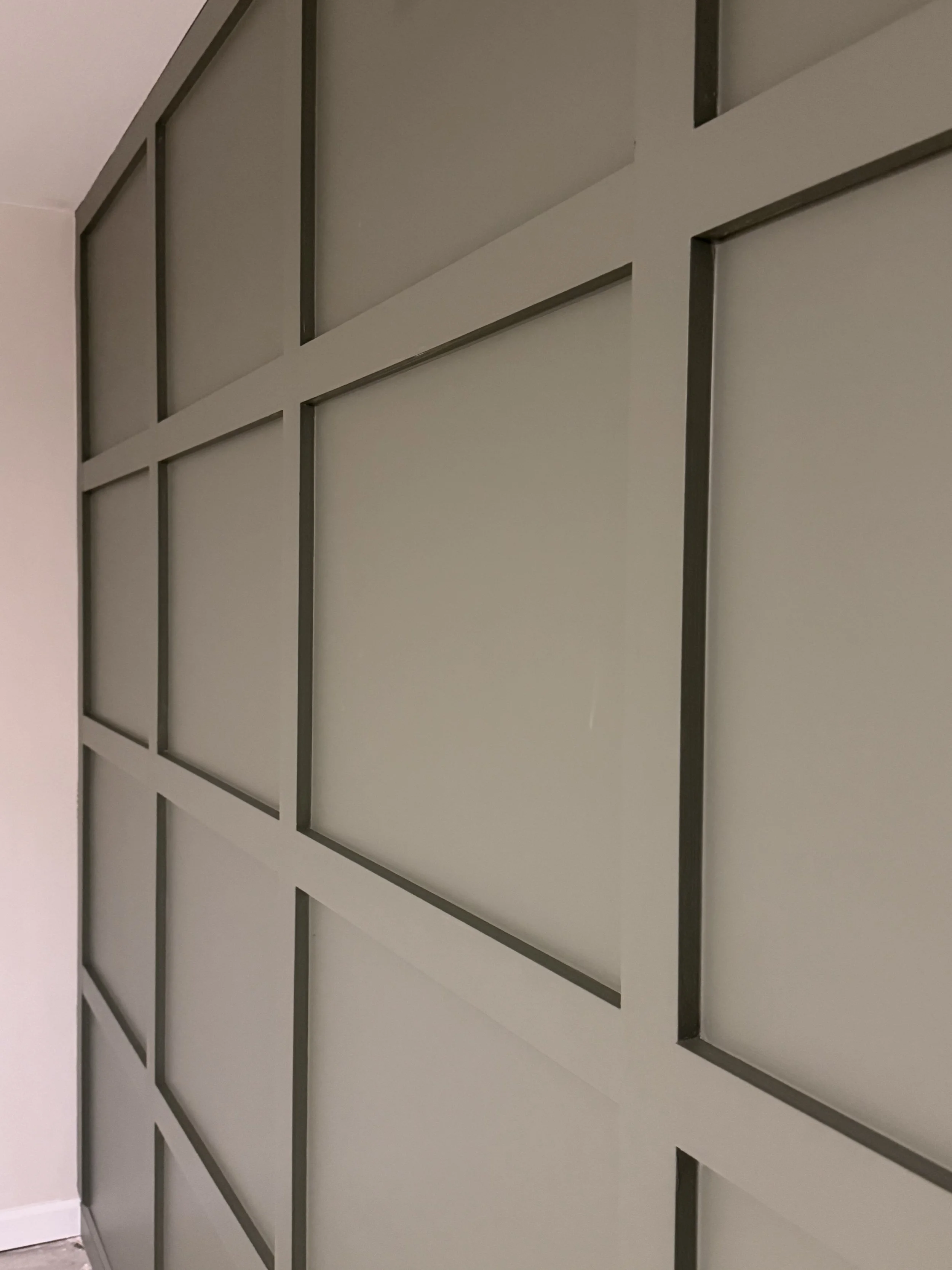 A built-in wall unit with sage framing and panels, divided into rectangular sections.