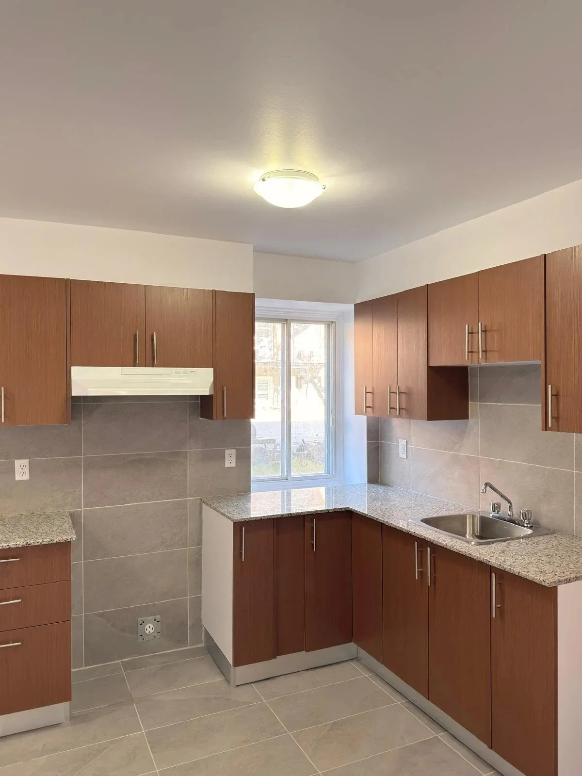 A kitchen with wooden cabinets, granite countertops, a stainless steel sink, a window above the sink, and a ceiling light fixture.