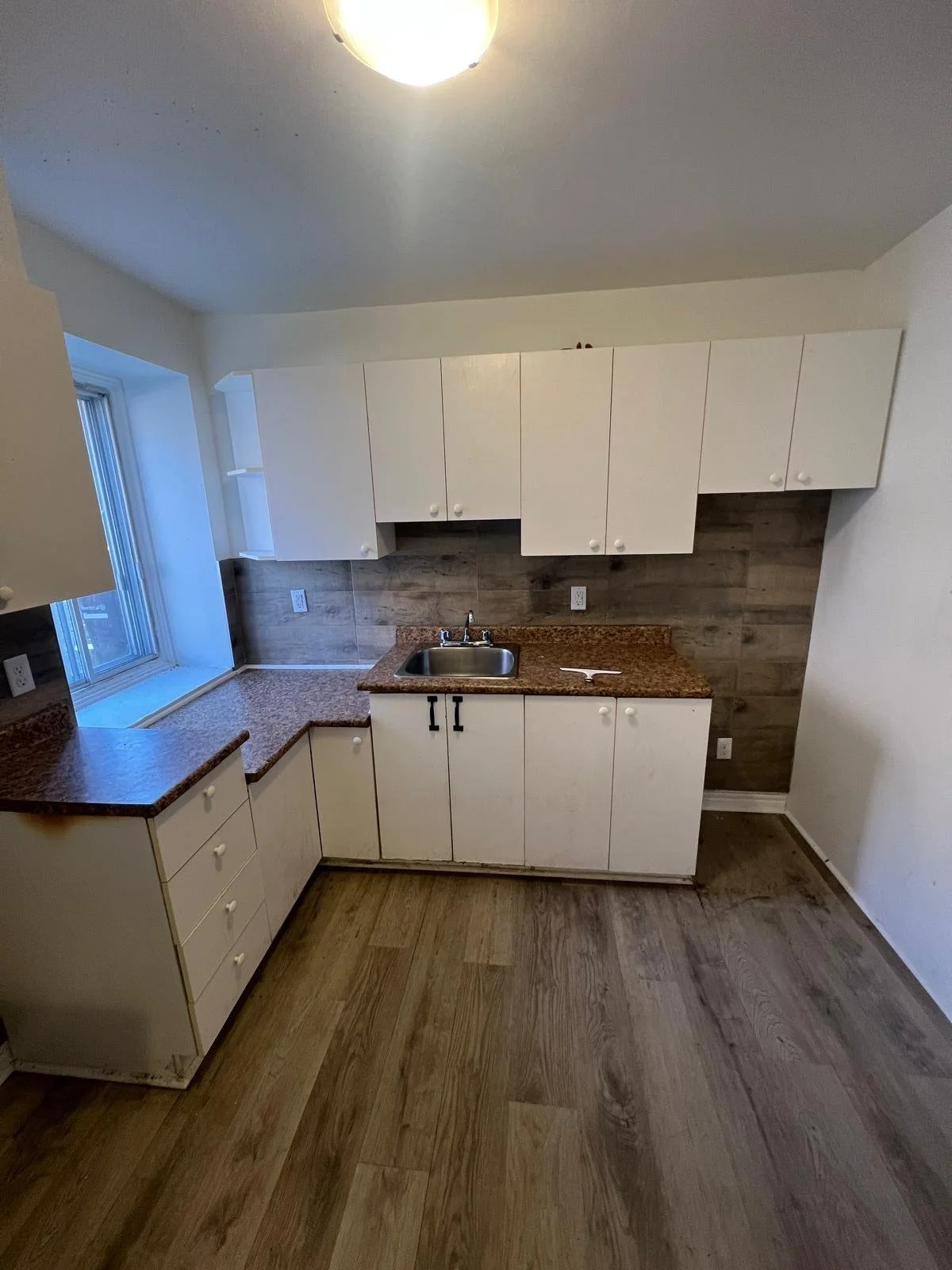 Kitchen with white cabinets, brown granite countertops, wood-look floor, and a window.