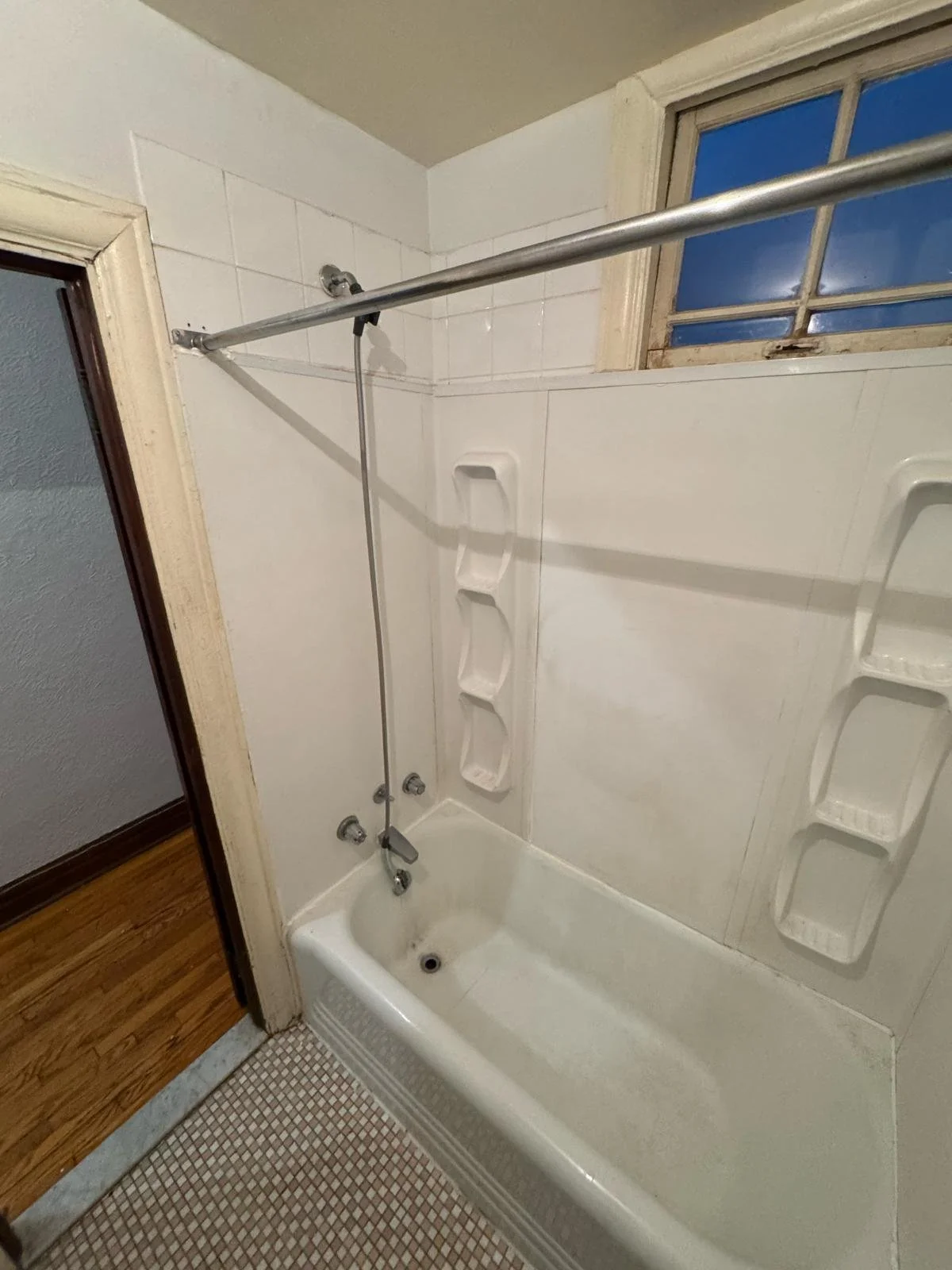 Small vintage bathtub with a showerhead, built-in shelves on the wall, a small window above, and a shower curtain rod.