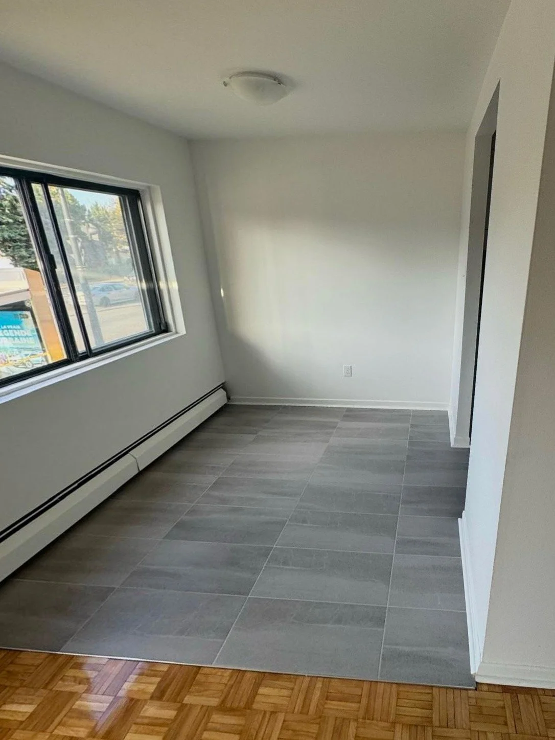 Empty room with large window, light gray tiled floor, white walls, and baseboard heater.