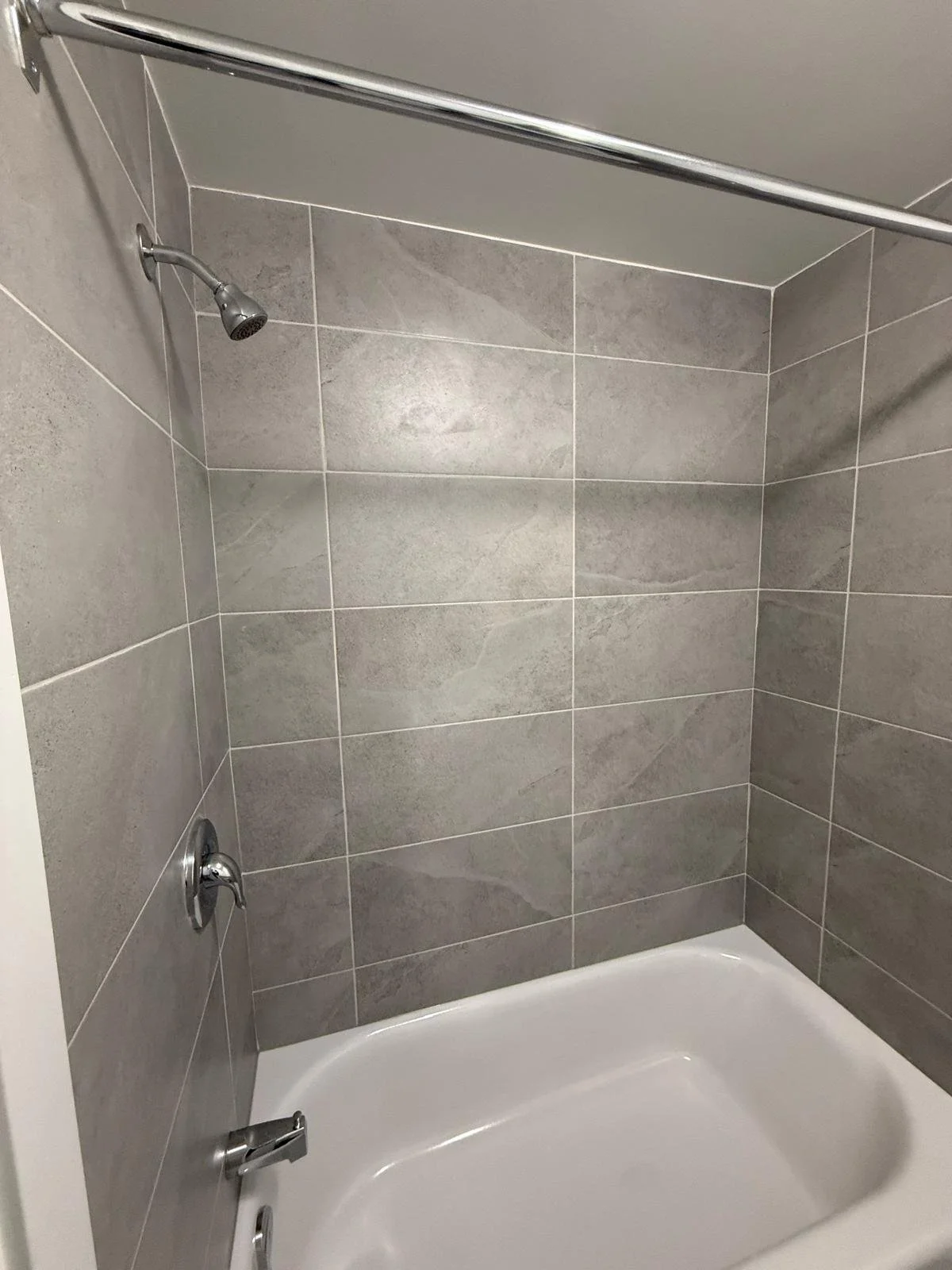 A bathtub in a bathroom with gray tile walls, a silver showerhead, and silver fixtures.