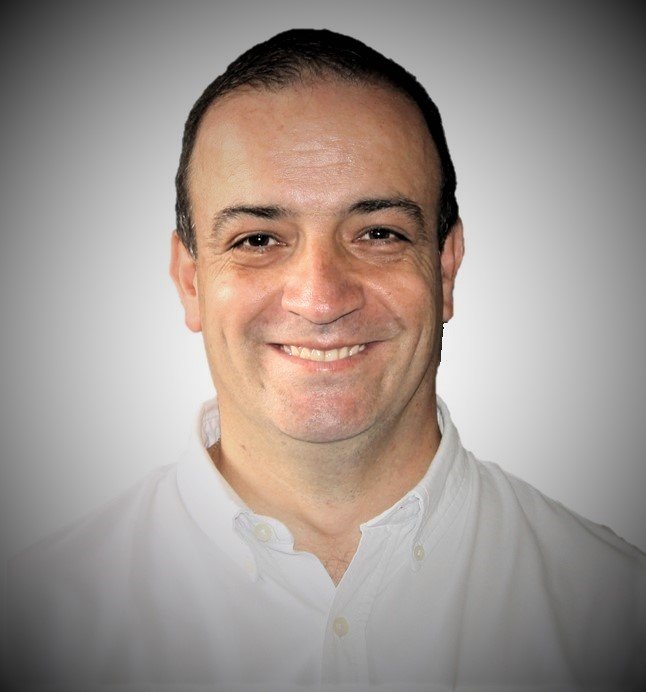 Retrato de un hombre sonriendo con camisa blanca, fondo gris graduado.