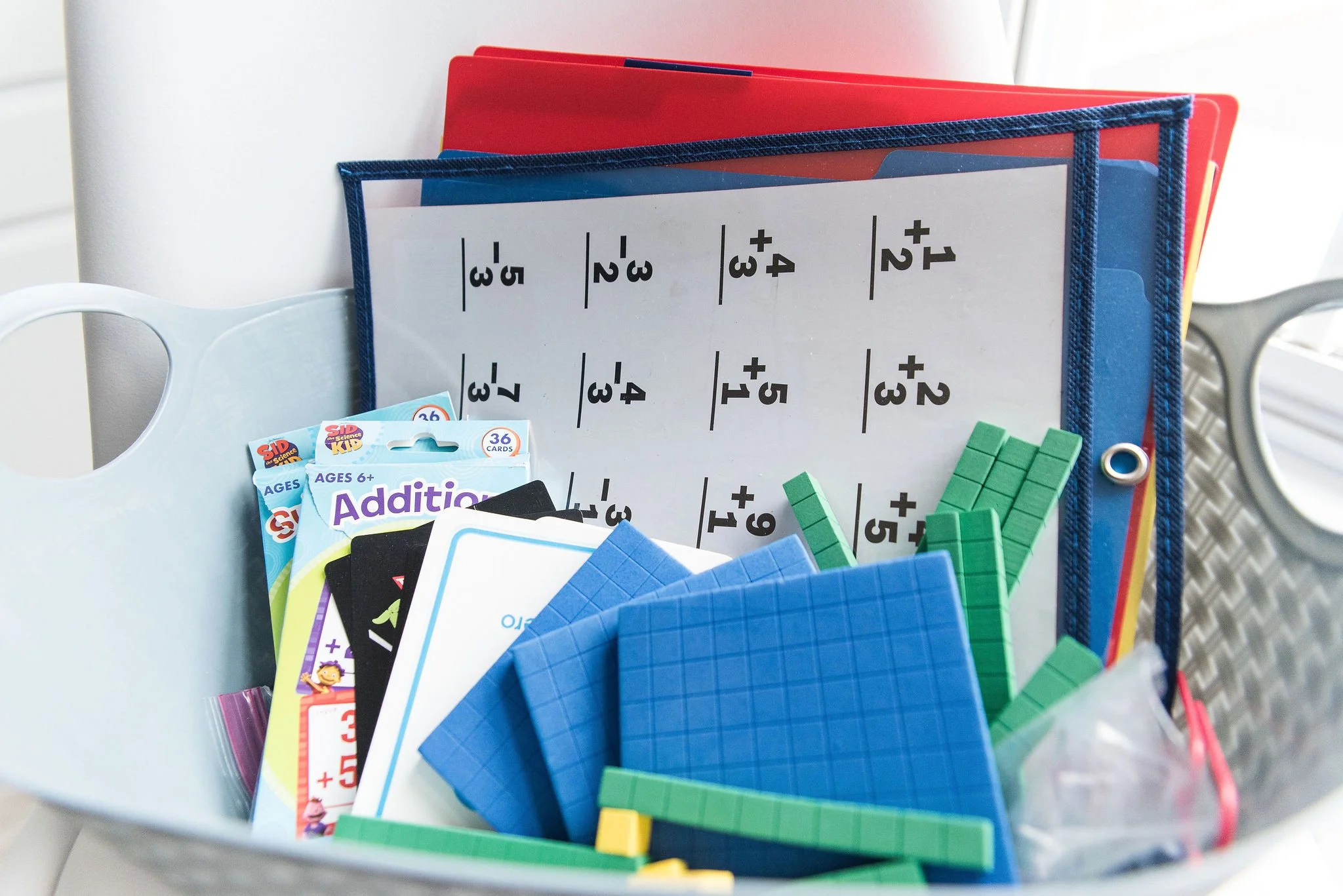 Educational supplies in a bucket, including addition flashcards, colorful counters, and a whiteboard with basic mathematics facts.