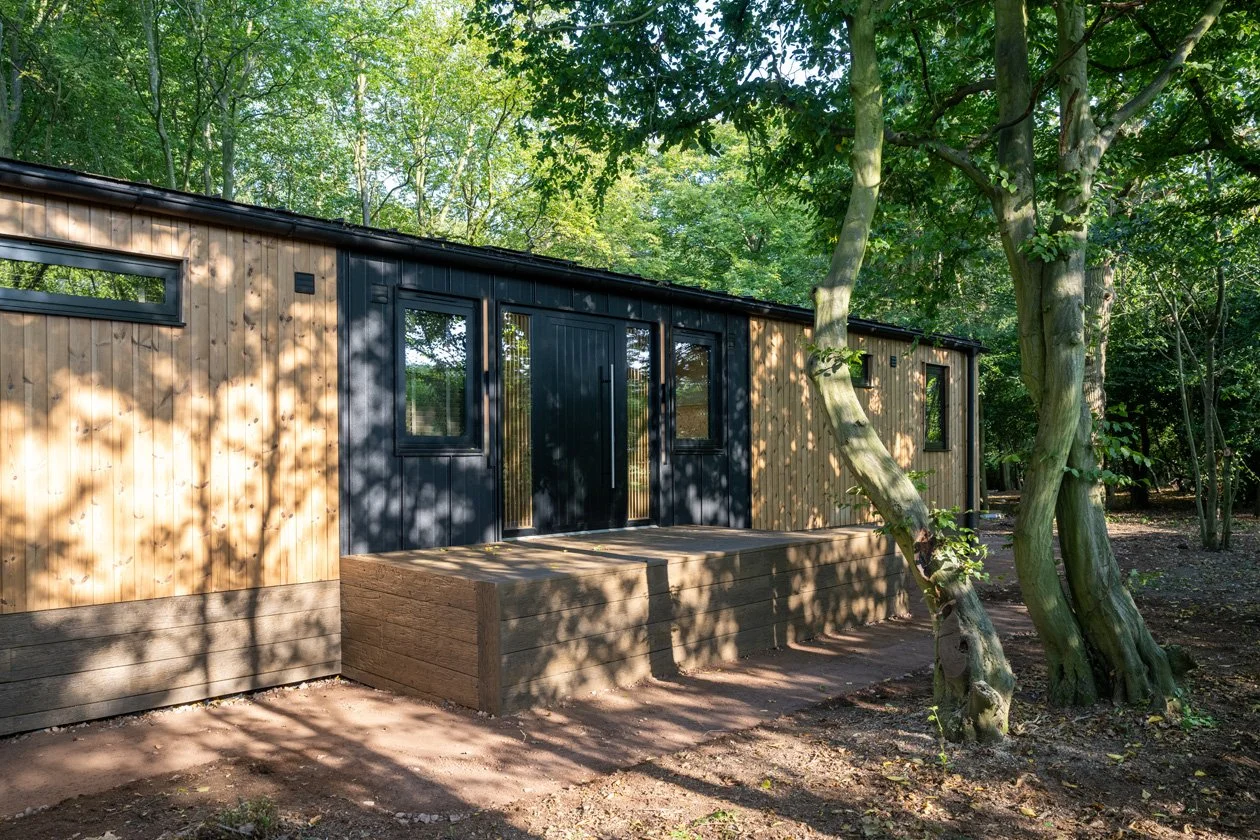 A modern tiny house with wooden exterior siding and black accents, situated among trees in a forested area, with a small wooden porch.