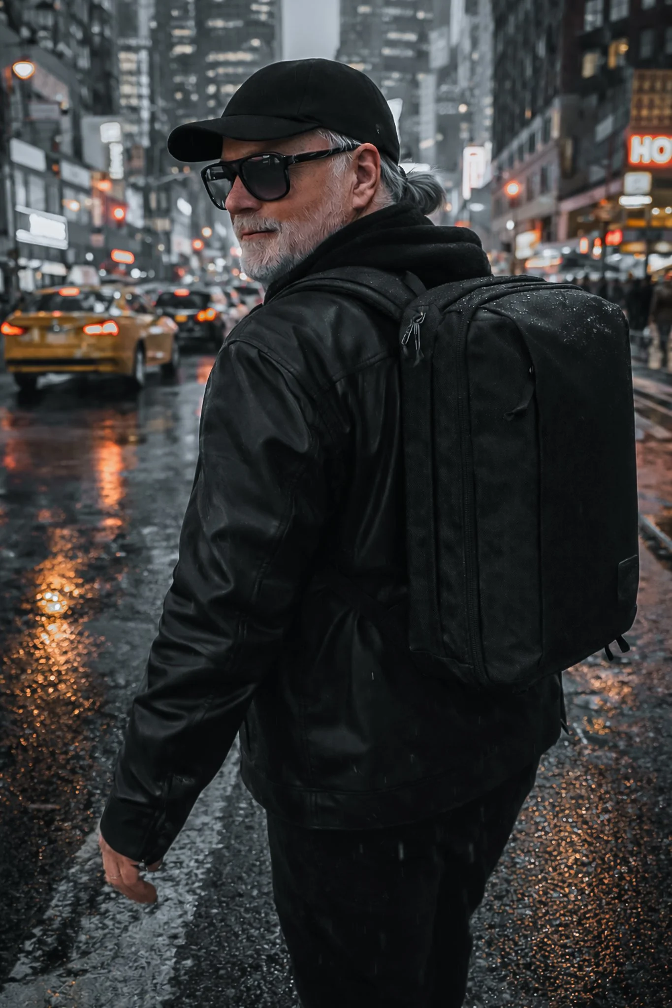 RC carrying a black backpack on a rainy New York City street at dusk