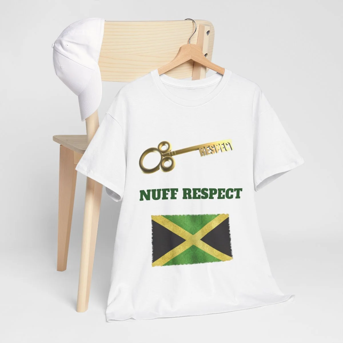 White T-shirt with gold key graphic, green text saying "NUFF RESPECT," and a Jamaican flag, hanging on a wooden hanger in front of a small wooden chair with a white cap draped over its back.