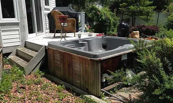 A hot tub on a backyard porch with outdoor furniture, plants, and garden in the background.
