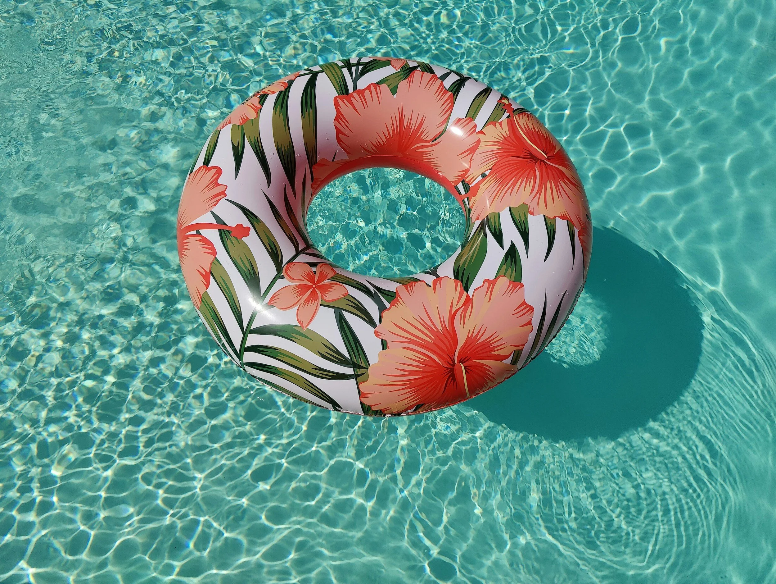 Inflatable pool float with a tropical flowers and leaves pattern, floating in a swimming pool.