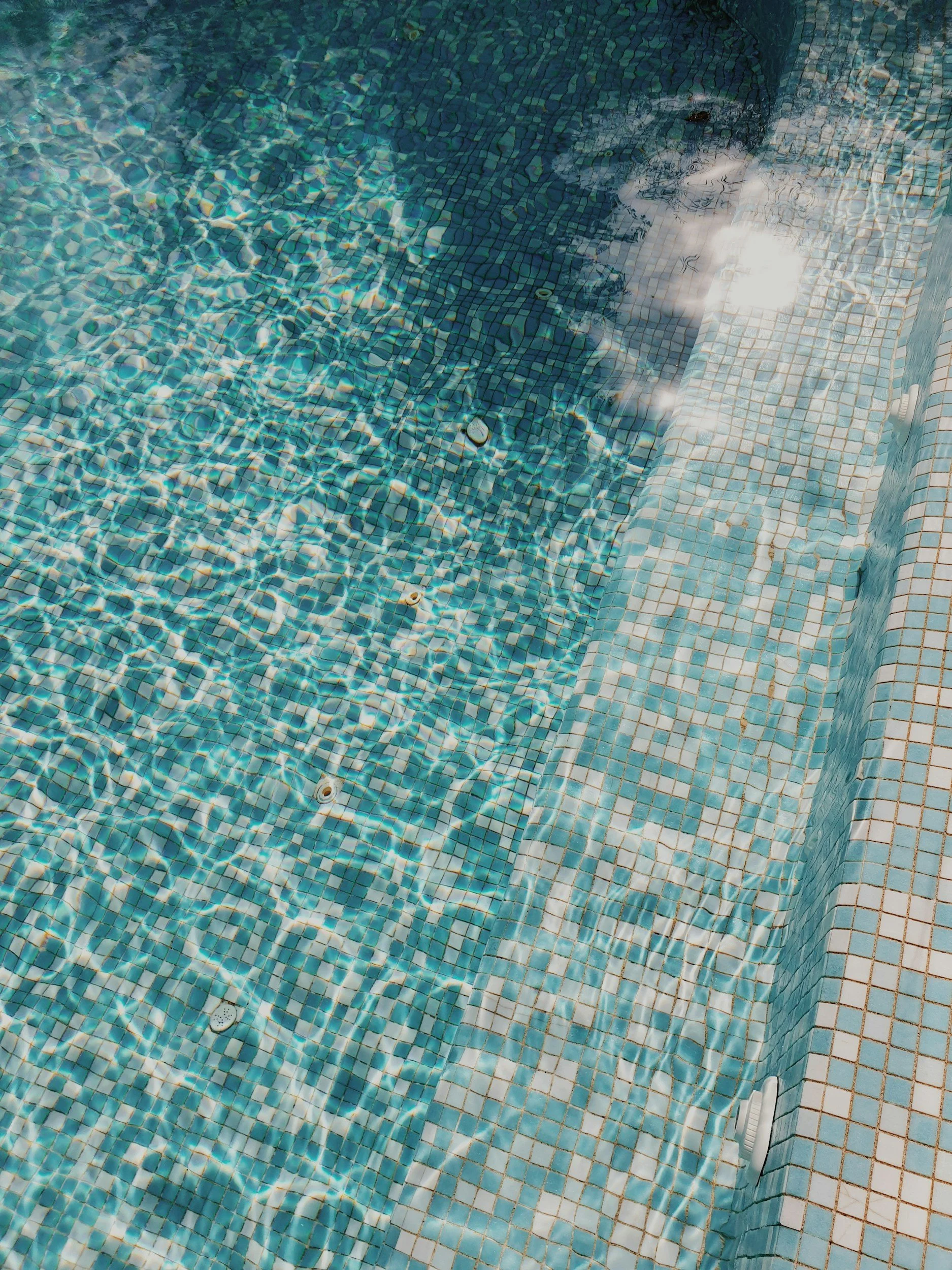 Person swimming underwater in a tiled pool with light reflecting off the water surface.