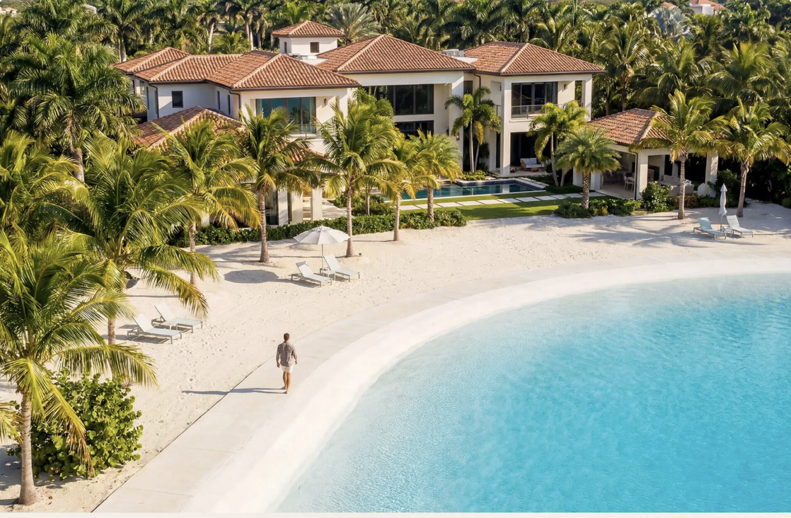 A woman walking along a paved pathway near a beach with lounge chairs, surrounded by palm trees and a large luxurious house with a tiled roof, pool, and lush landscaping.
