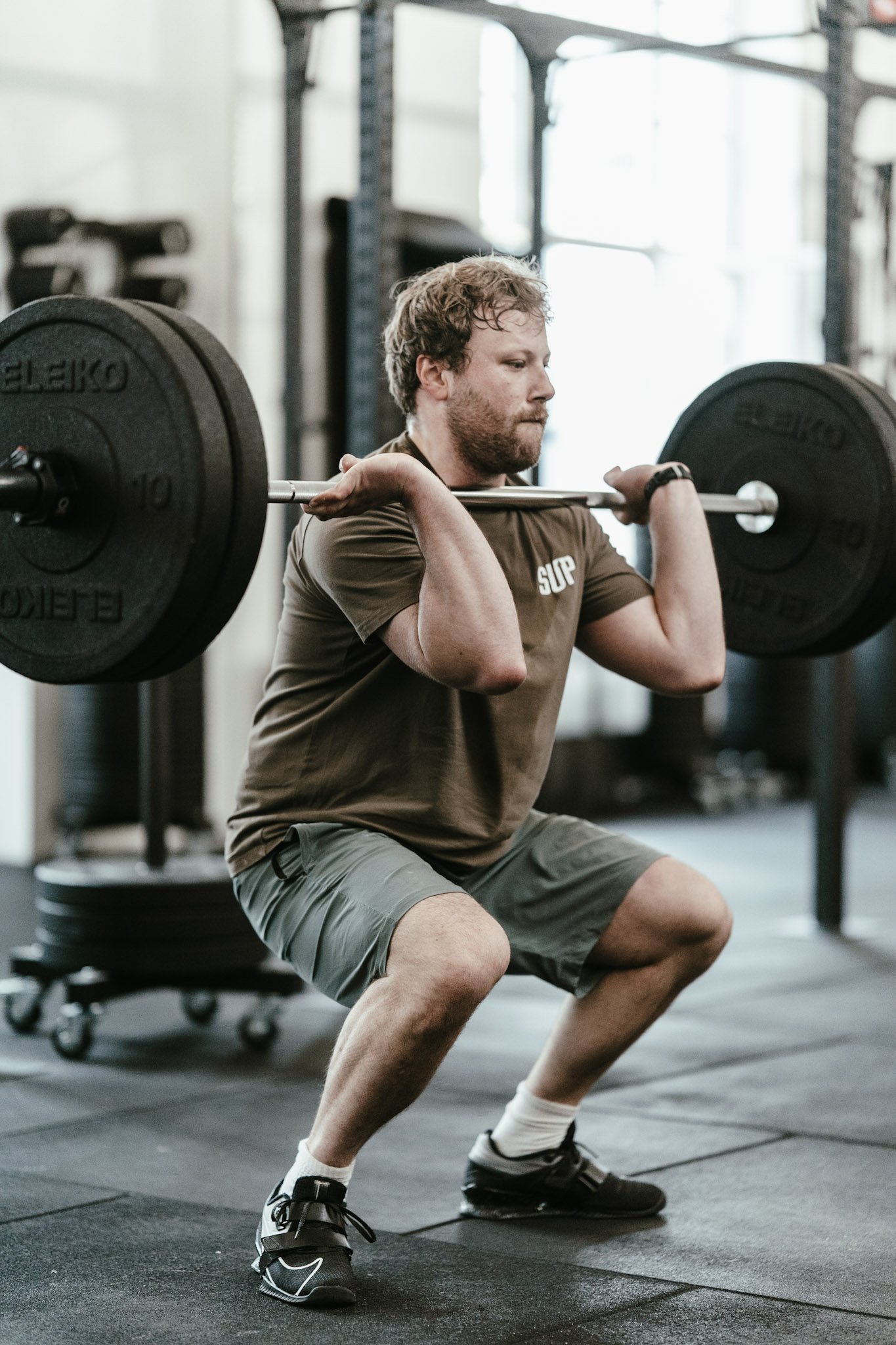 Mann beim Kniebeugen mit Langhantel im Fitnessstudio.
