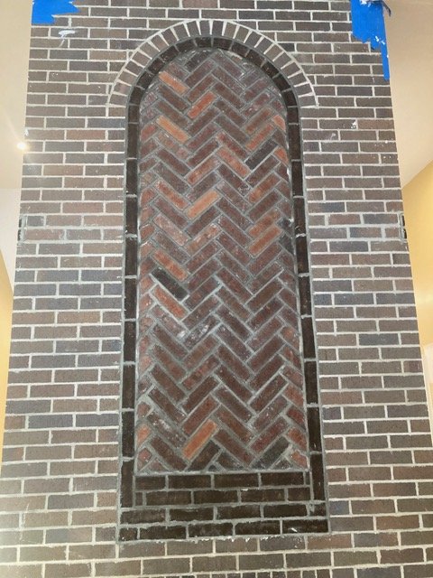 Brick wall with an arched recessed decorative brick pattern in the center.