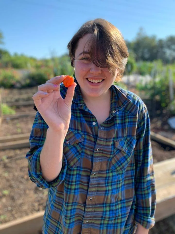 Cee holding an orange habenero pepper