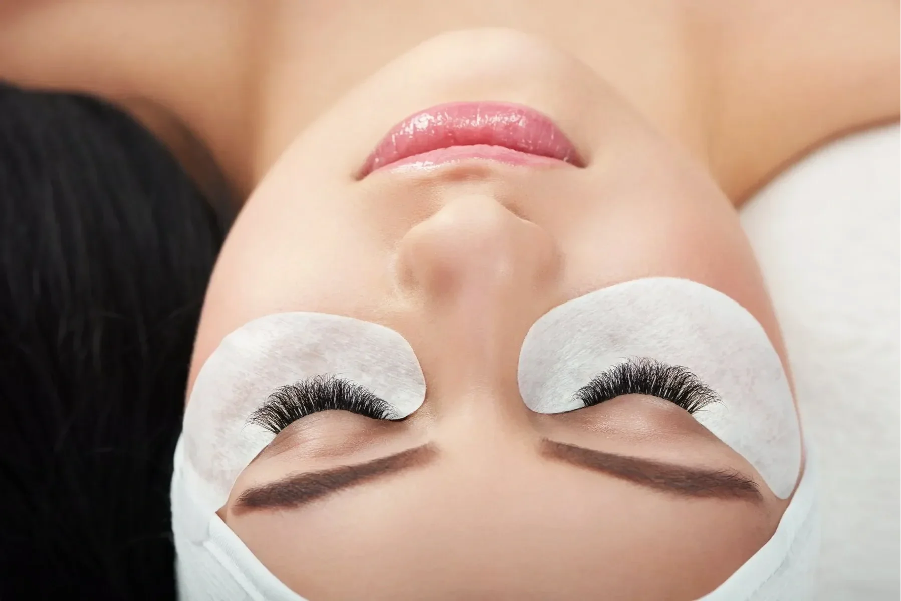 Persona recibiendo tratamiento de belleza en los ojos, con parches blancos y cabello oscuro.