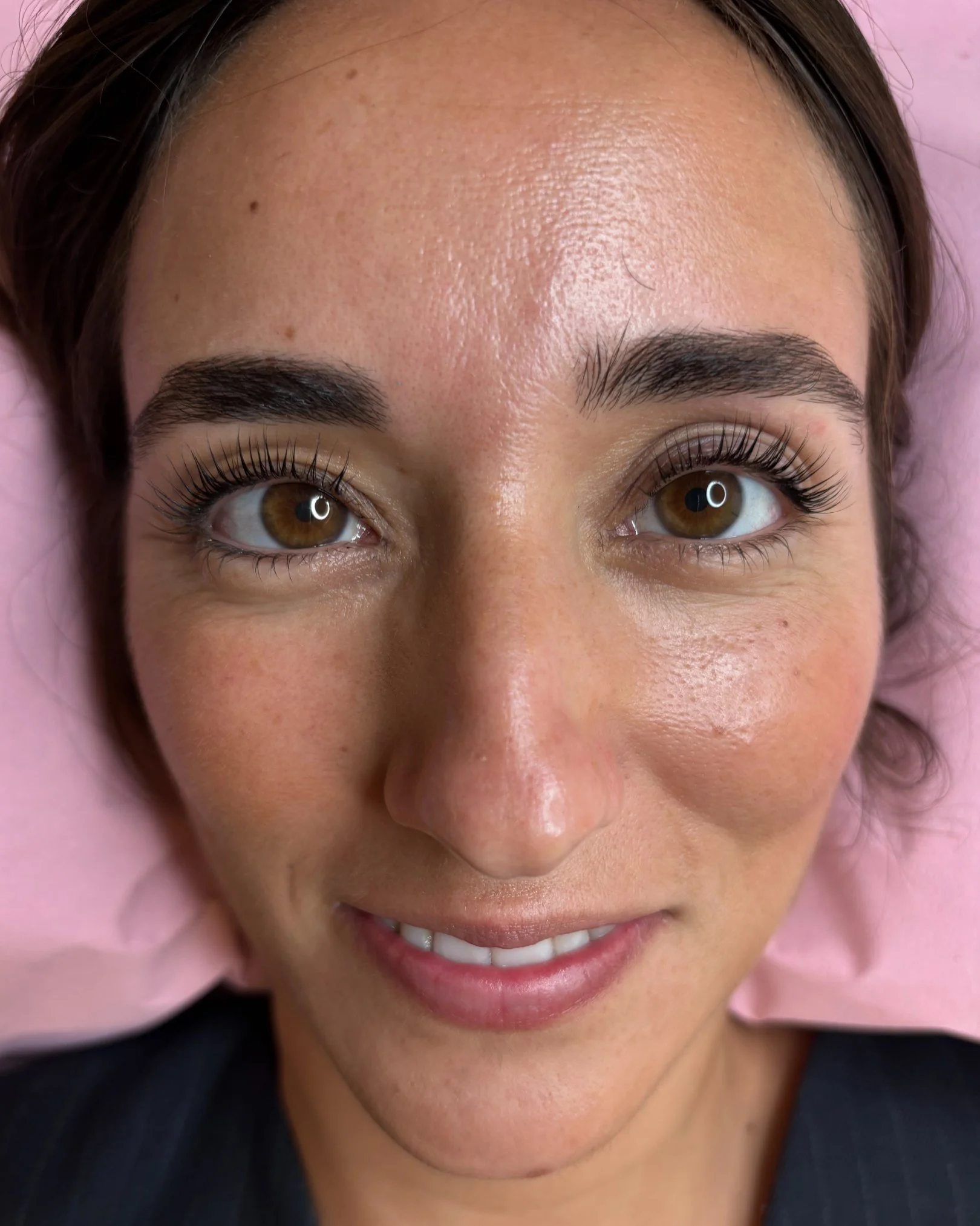 Rostro de una mujer con cejas arregladas, ojos marrones y una sonrisa, en un entorno de consulta médica o estética.